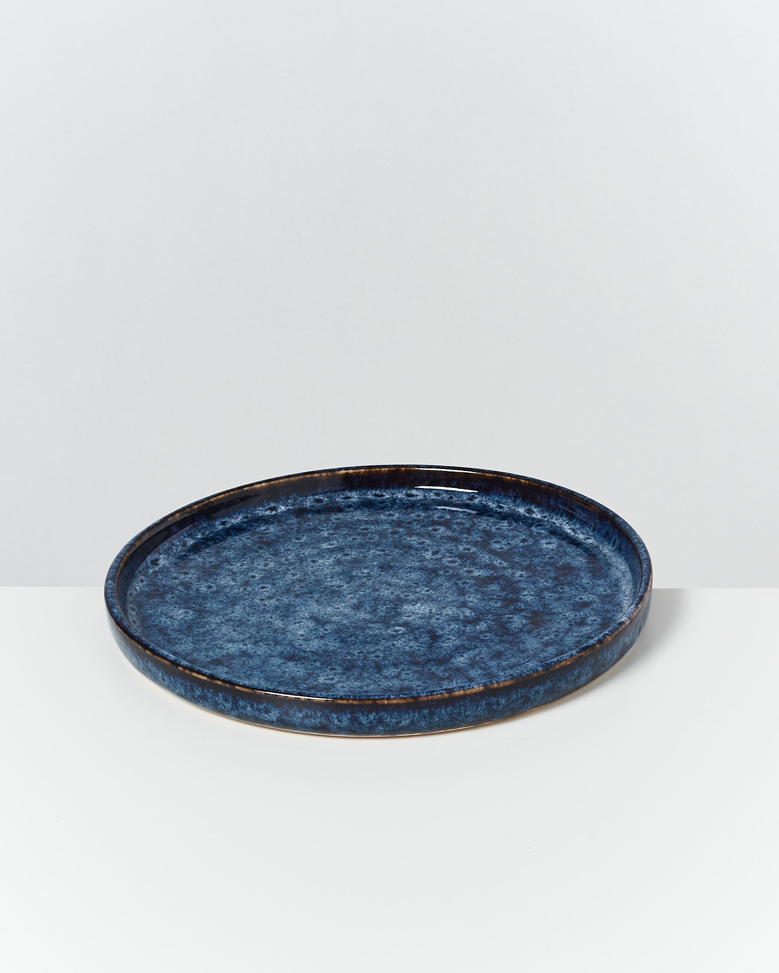 Blauer Keramikteller mit glatter Oberfläche auf weißem Hintergrund.