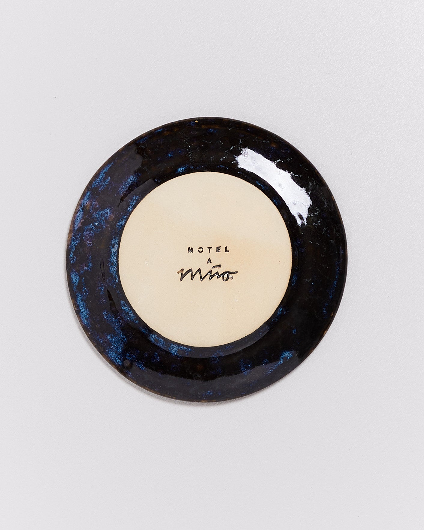 Runder Keramikteller mit dunkelblauem Rand und beigefarbenem Zentrum mit der Aufschrift: "Motel a Miro."