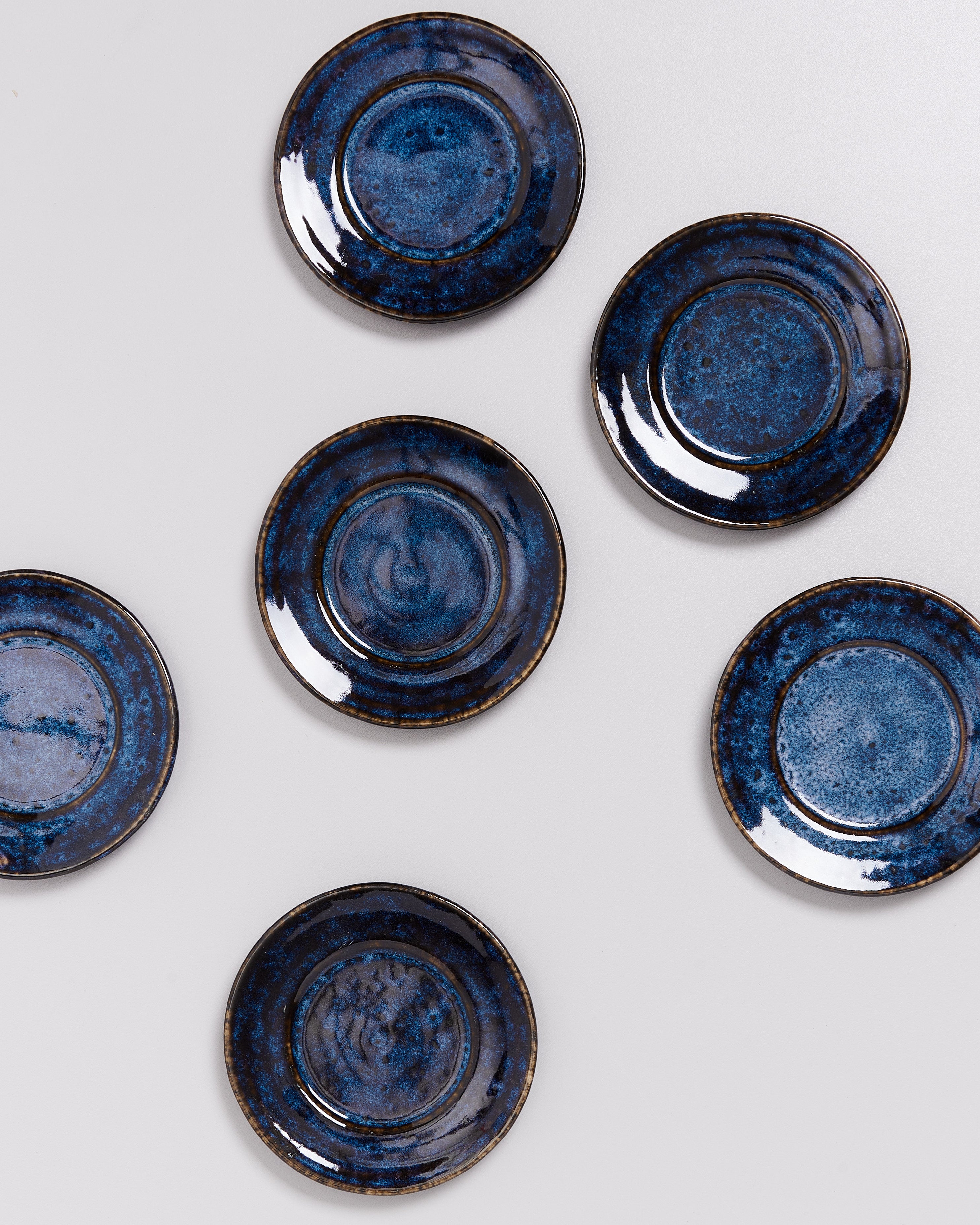 Sechs blaue Keramikteller mit unregelmäßigen Mustern sind auf einer hellen Oberfläche angeordnet.