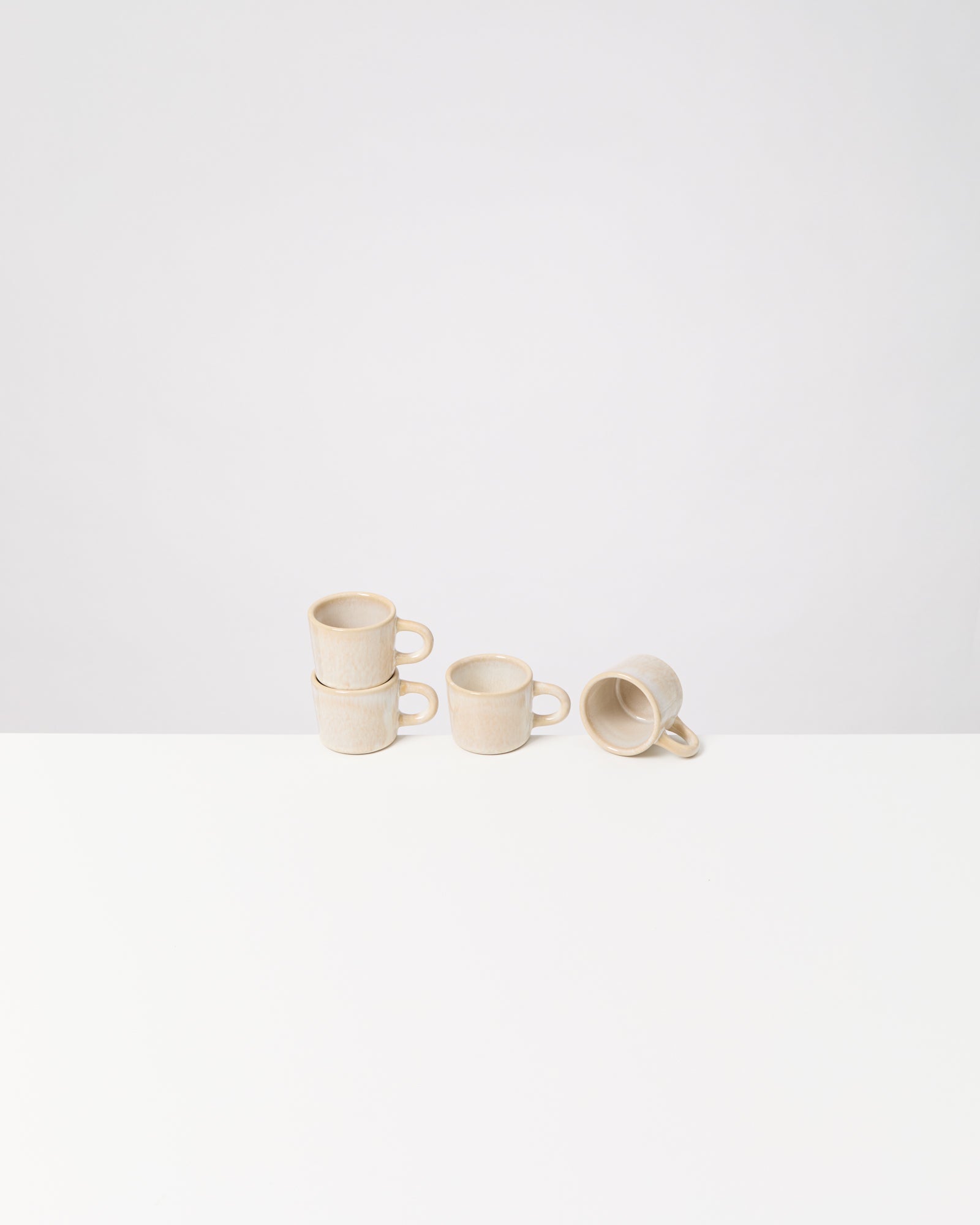 Vier stapelbare beige Tassen auf einem weißen Tisch, eine davon liegt auf der Seite.