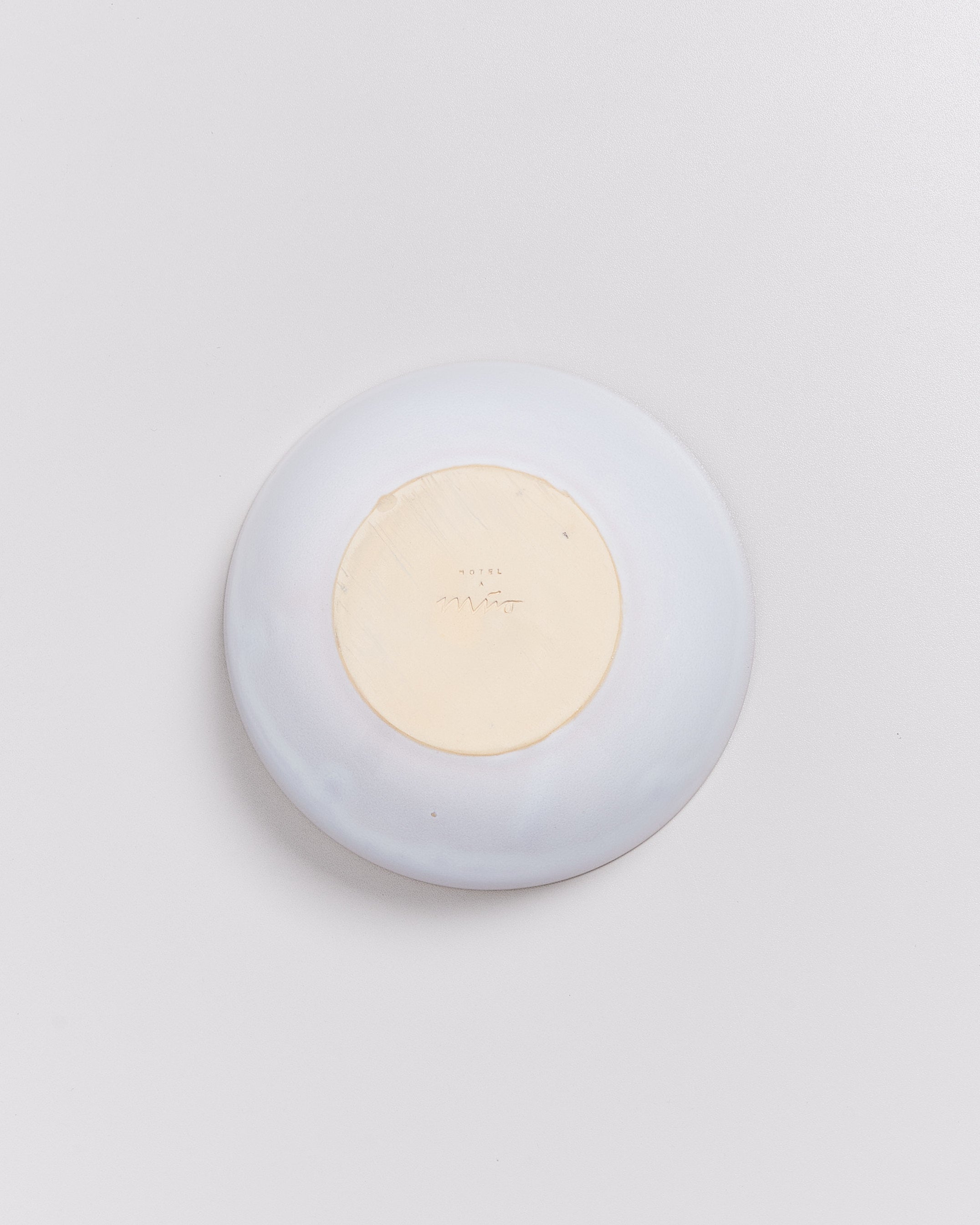 Weiße Schale, von oben gesehen, mit beiger, beschrifteter Unterseite auf weißem Hintergrund.