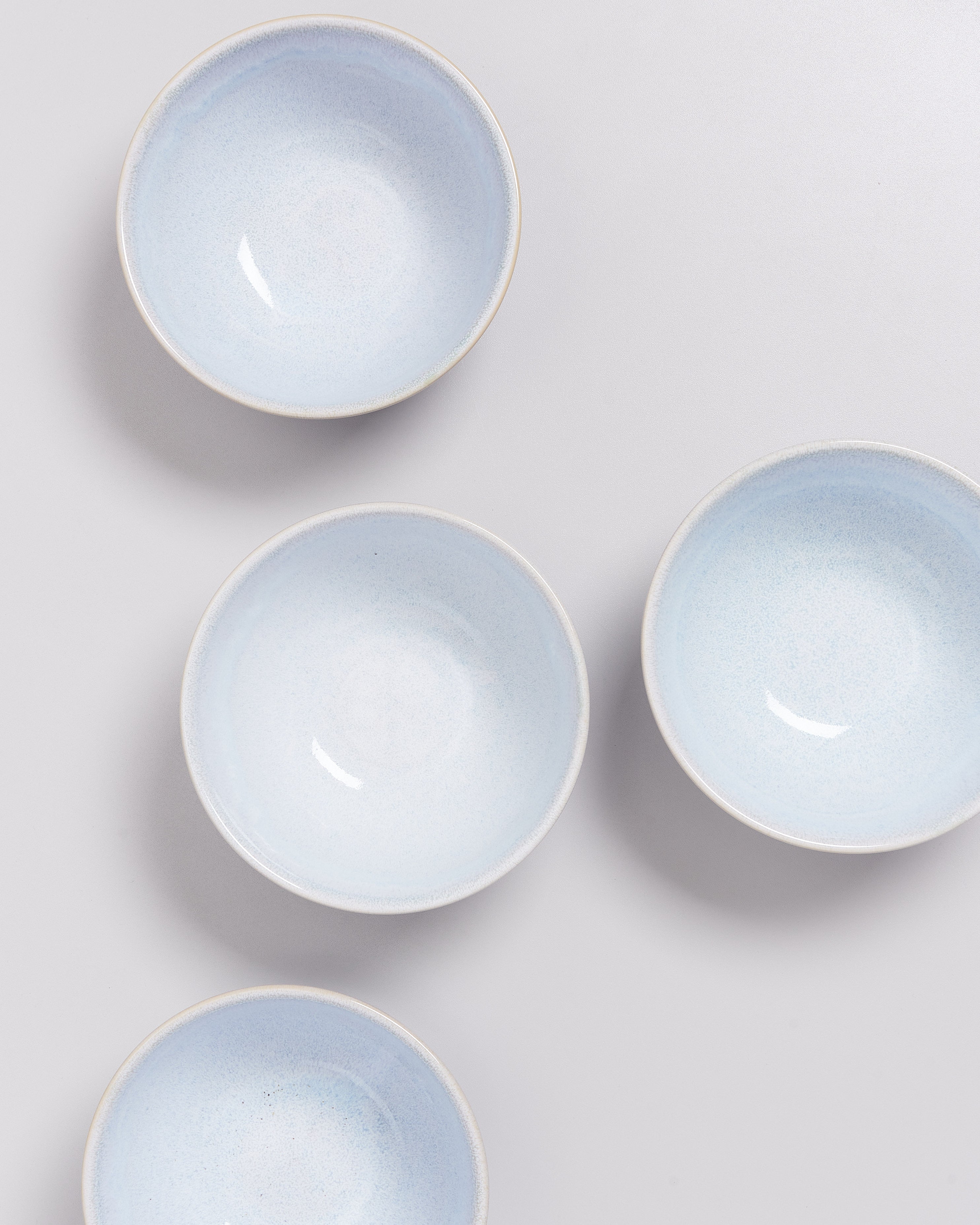 Vier helle, blau-weiße Keramikschalen sind auf einer grauen Oberfläche verteilt angeordnet.