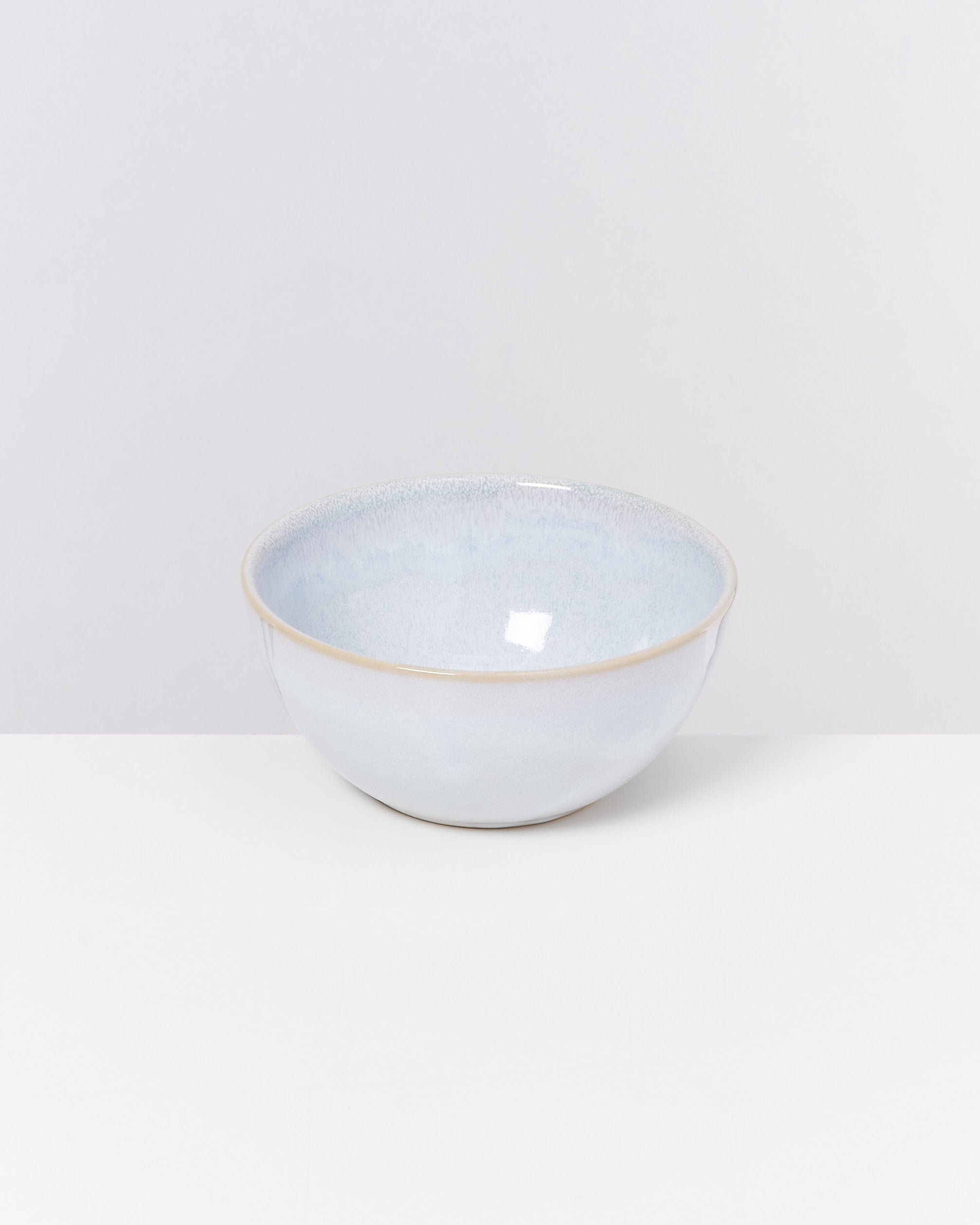 Eine weiße Keramikschale mit einem dezenten blauen Schimmer steht auf einem weißen Tisch vor einem weißen Hintergrund.
