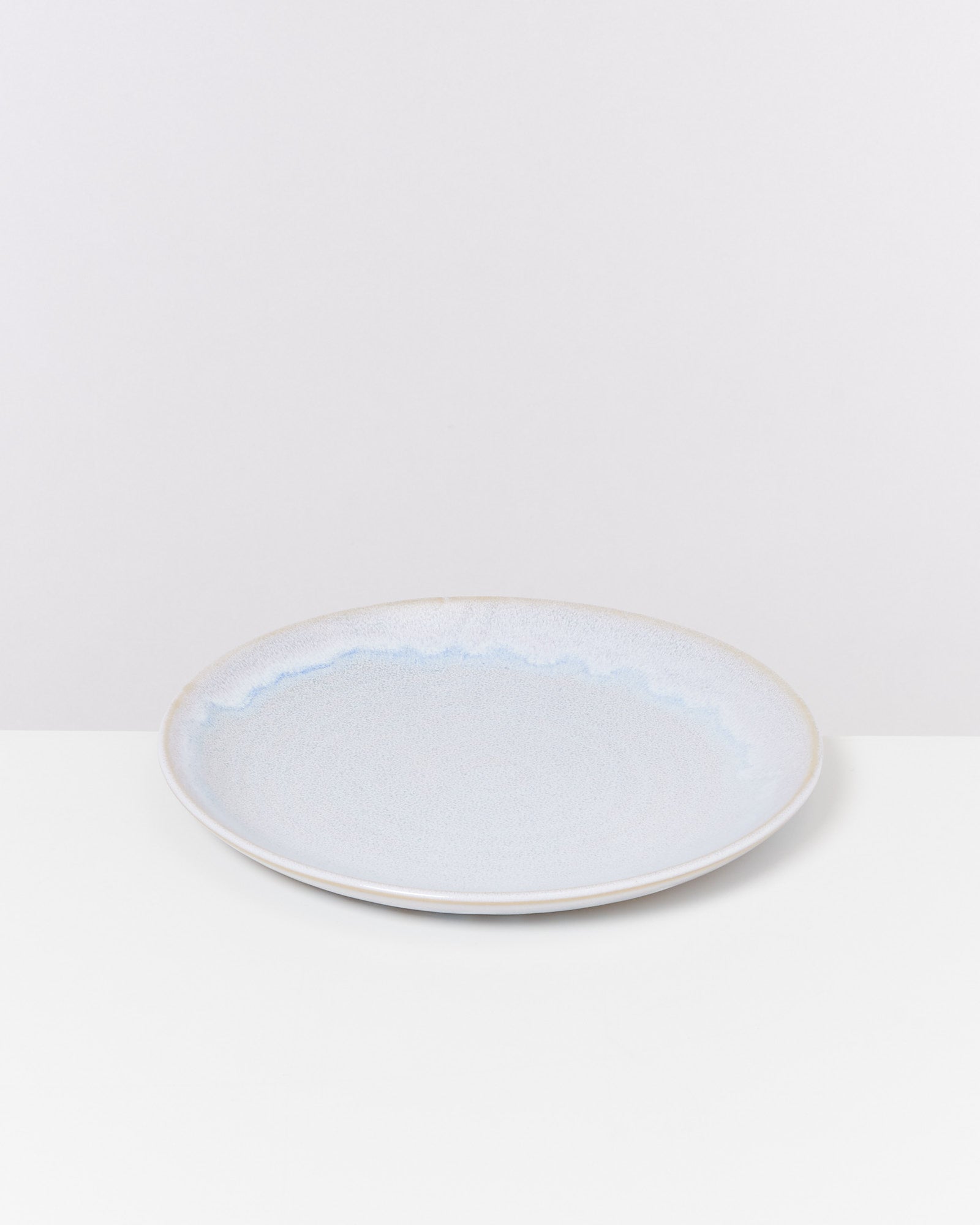 Blauer Keramikteller mit leichtem Wellendesign auf weißer Oberfläche vor weißem Hintergrund.