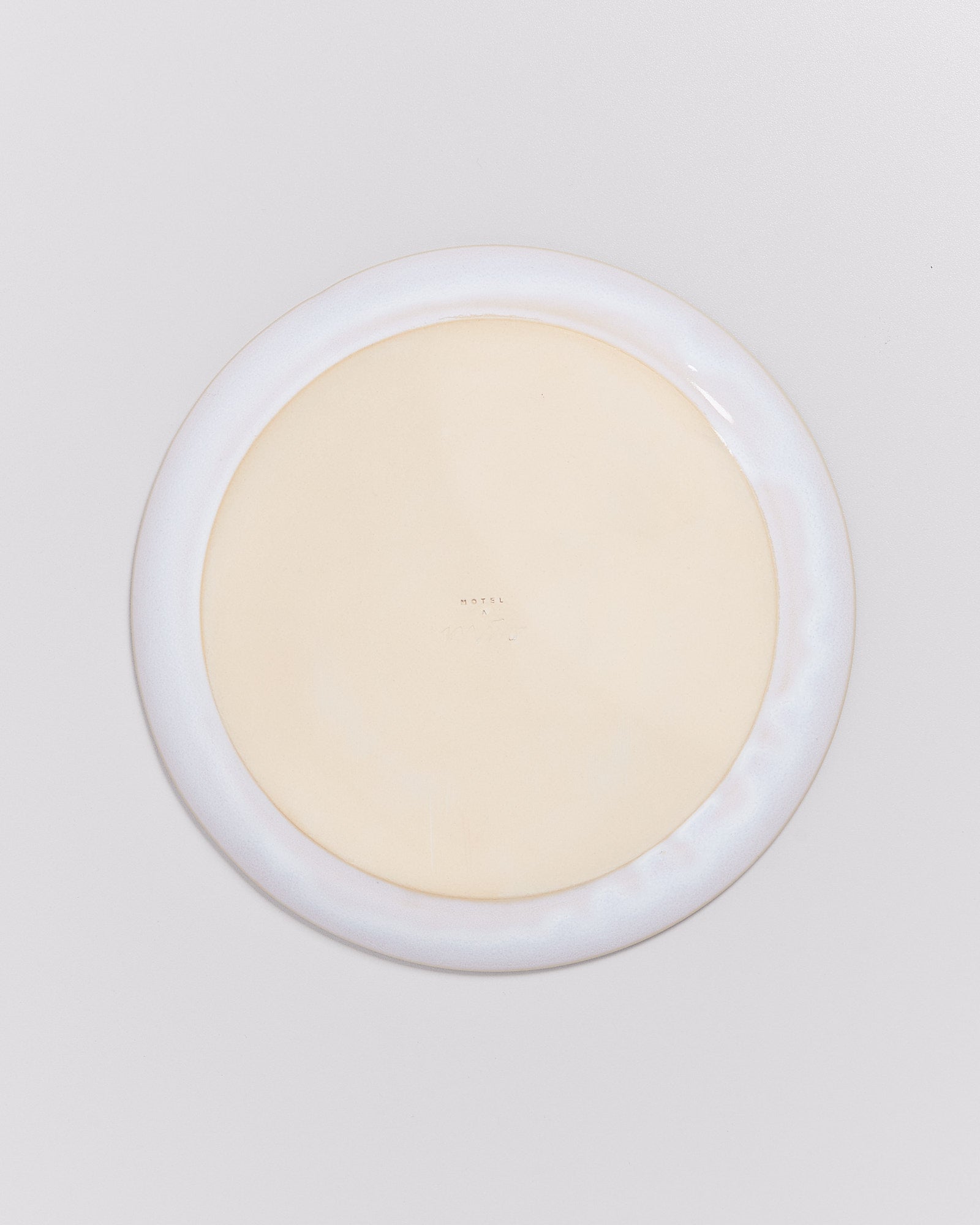 Rückseite eines weißen Tellers mit leicht gelblichem Zentrum und kleiner Prägung in der Mitte.