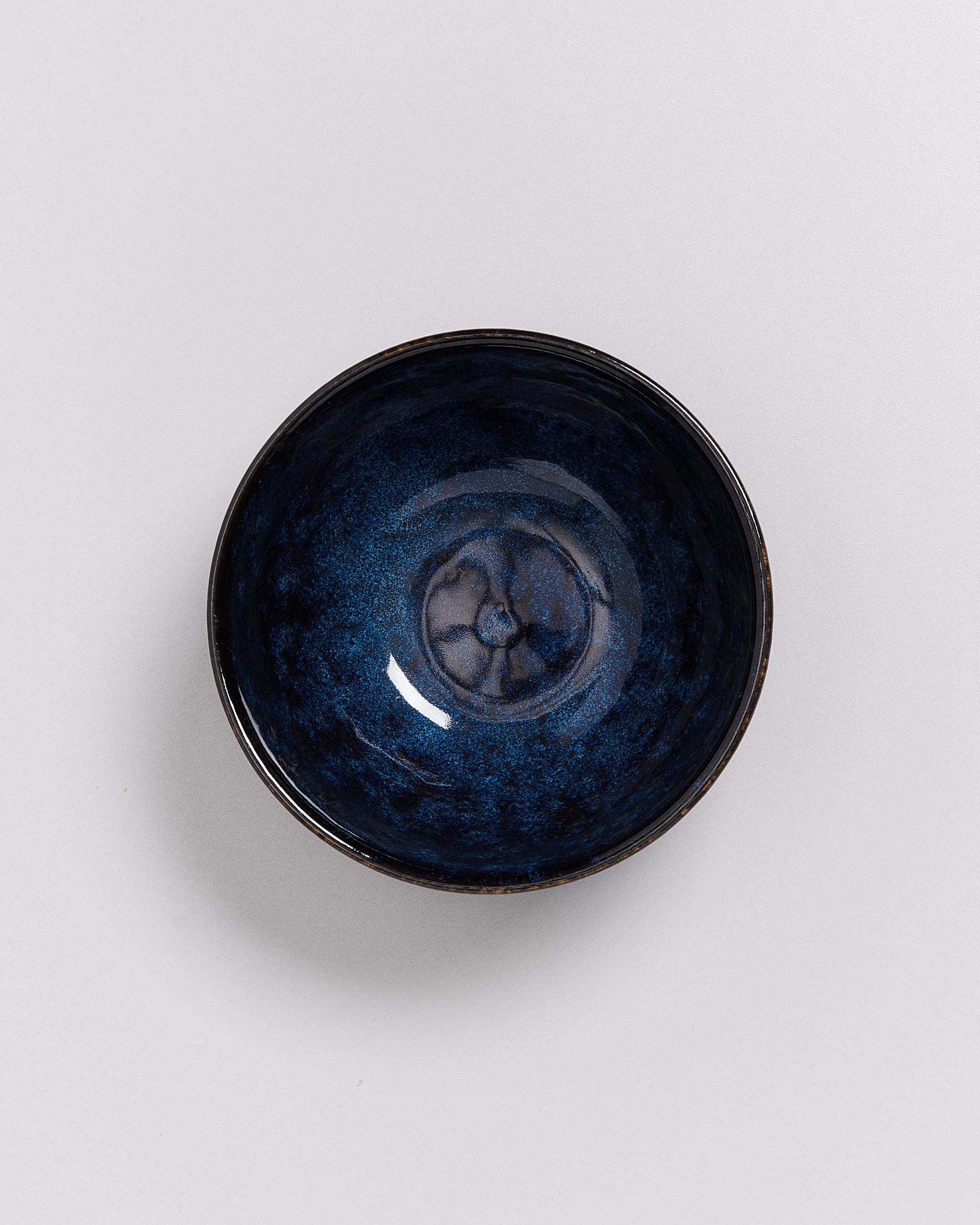 Dunkelblaue, glänzende Keramikschale mit kunstvollem Muster auf hellem Hintergrund.