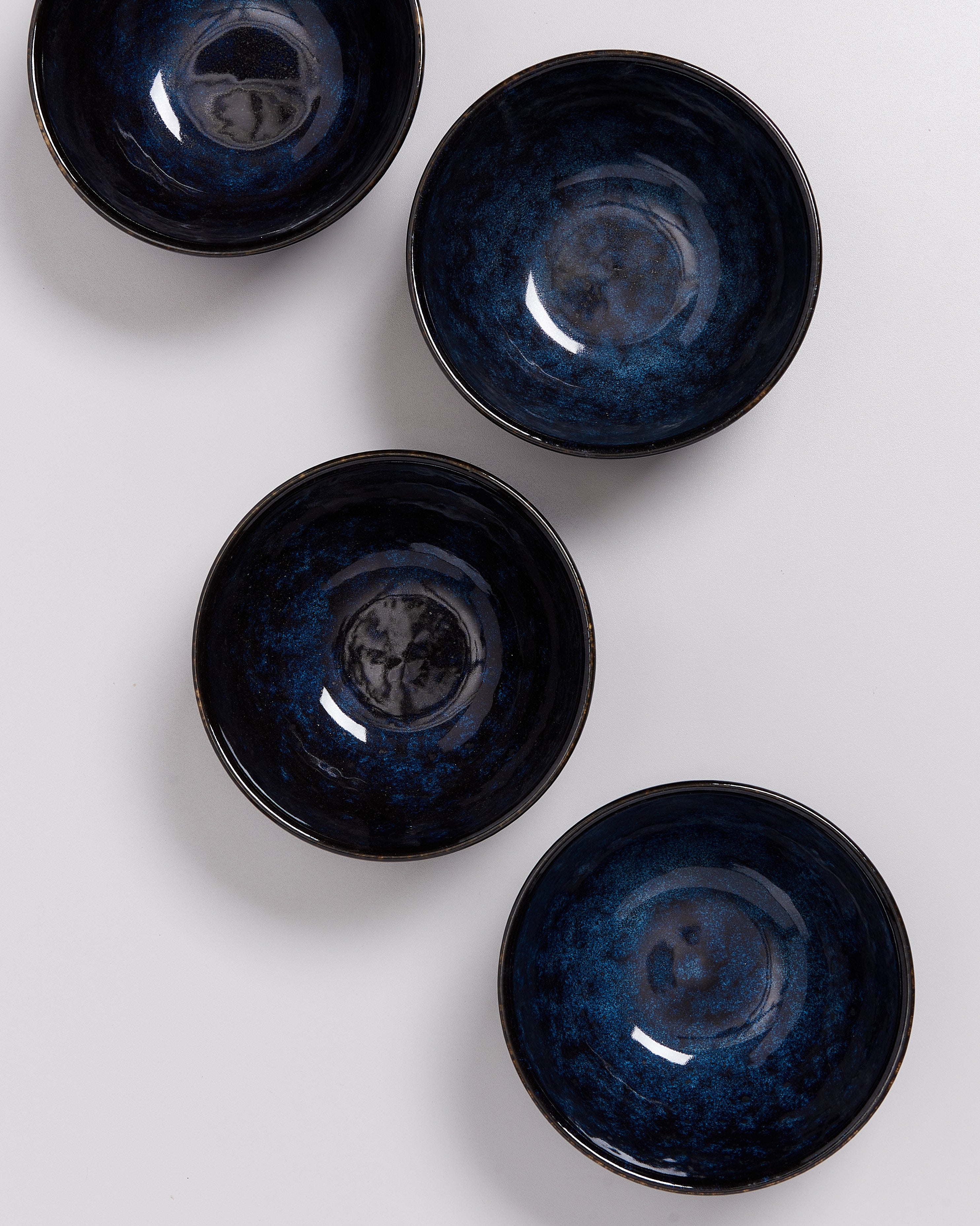 Vier blaue Keramikschalen mit glänzender Oberfläche liegen auf einer weißen Fläche.