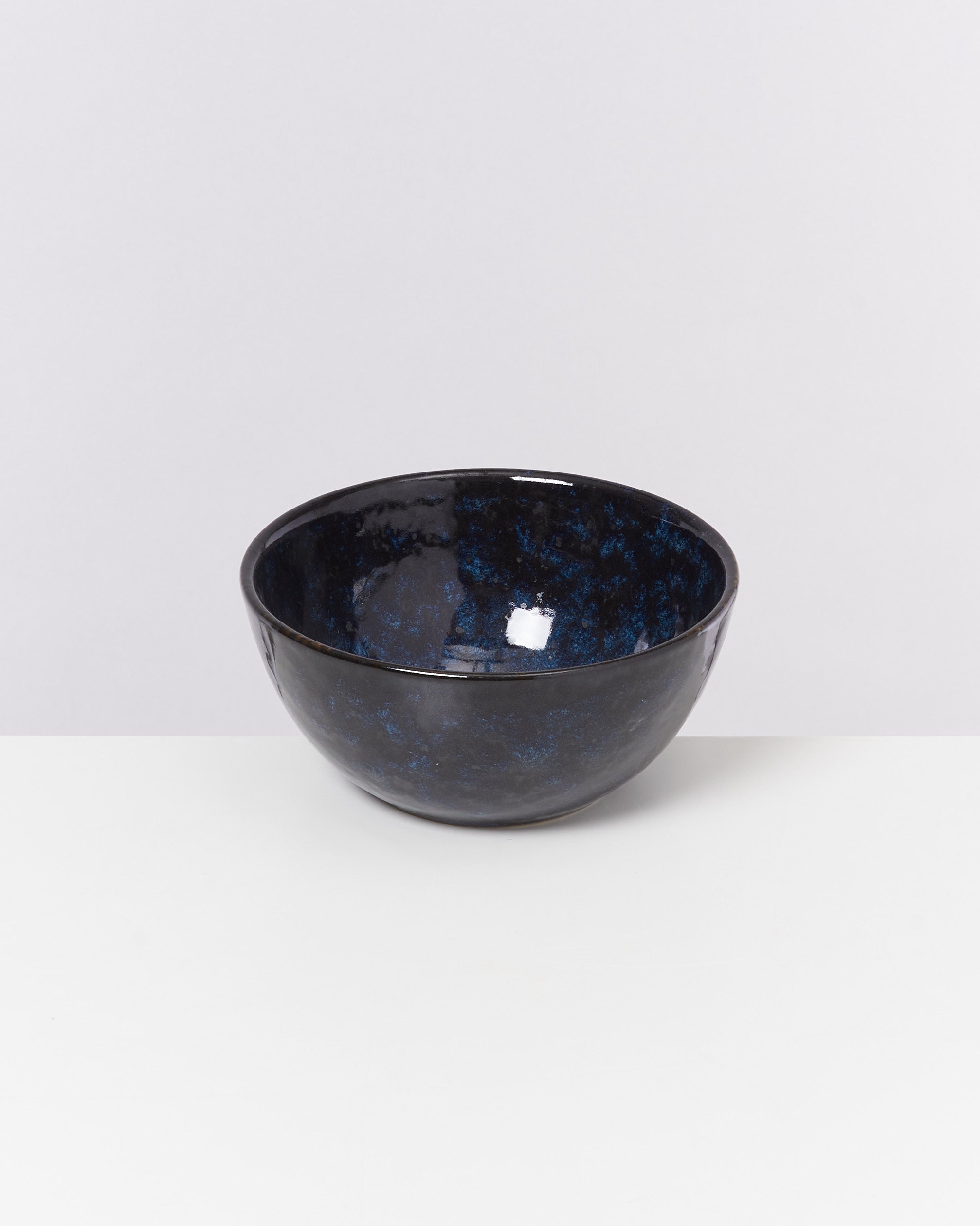 Schwarze Keramikschale mit blauen Tupfen auf weißem Hintergrund.