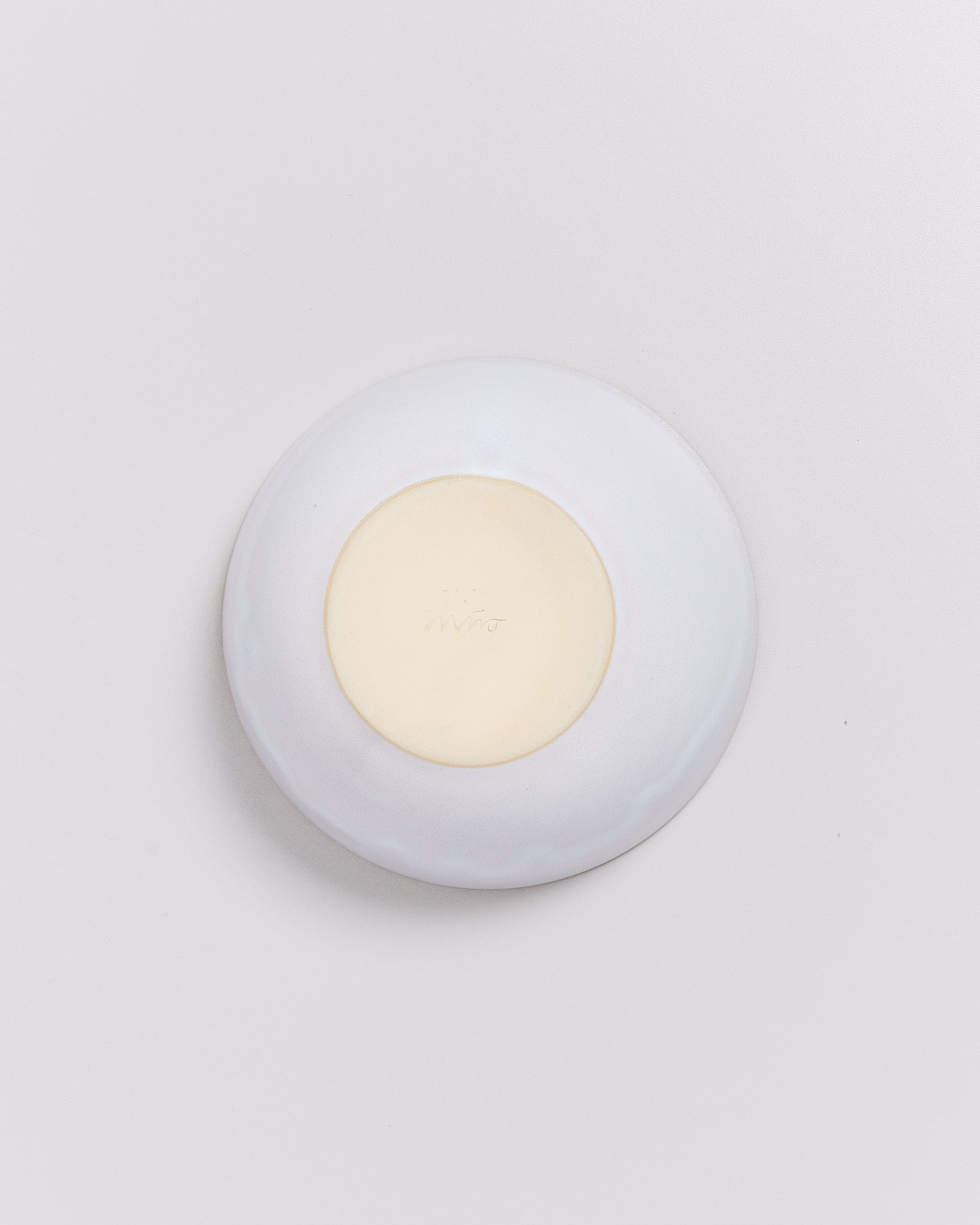 Ein runder, heller Keramikteller auf einer weißen Oberfläche, von oben fotografiert.