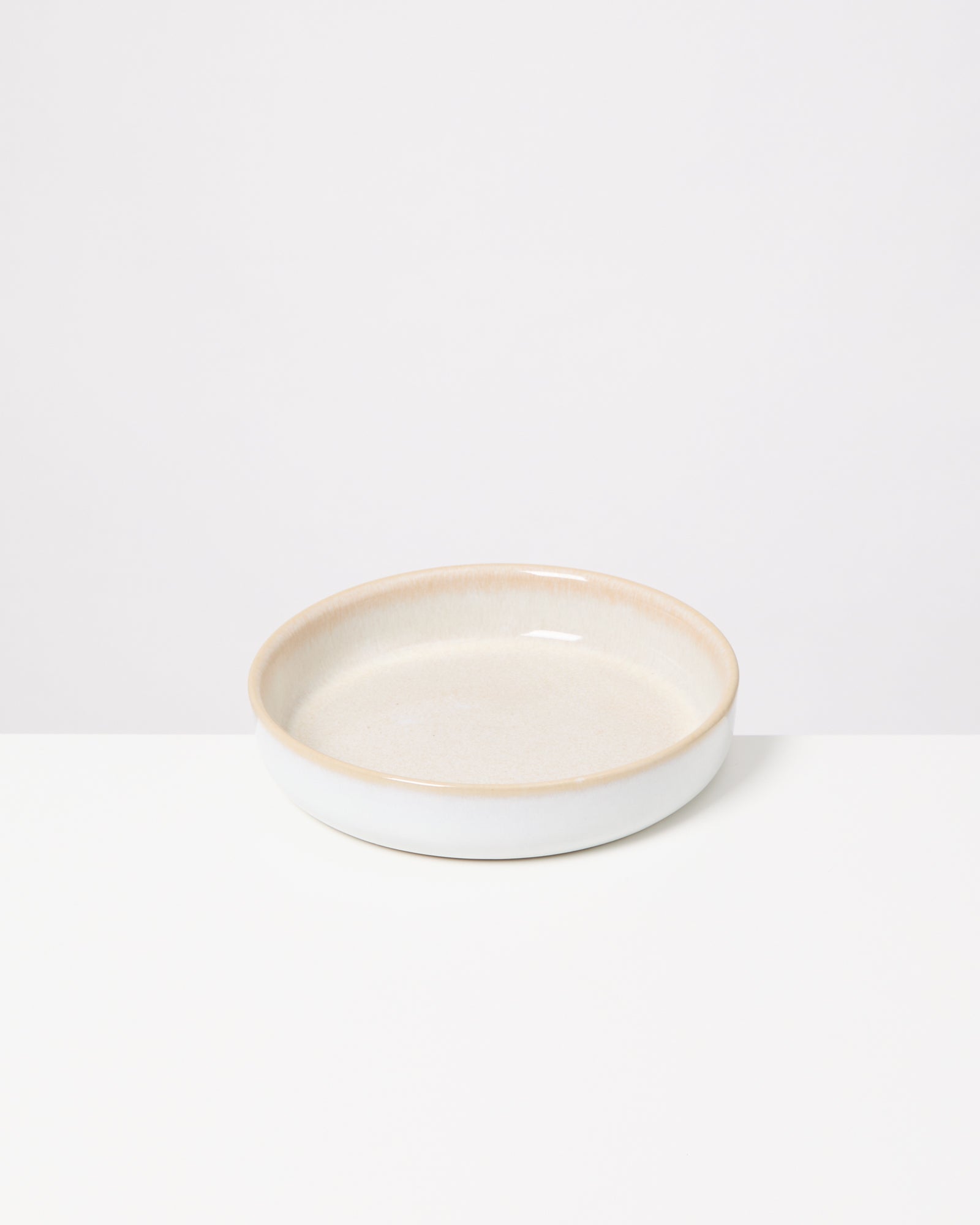 Flacher, runder, cremefarbener Keramikteller auf weißem Hintergrund.