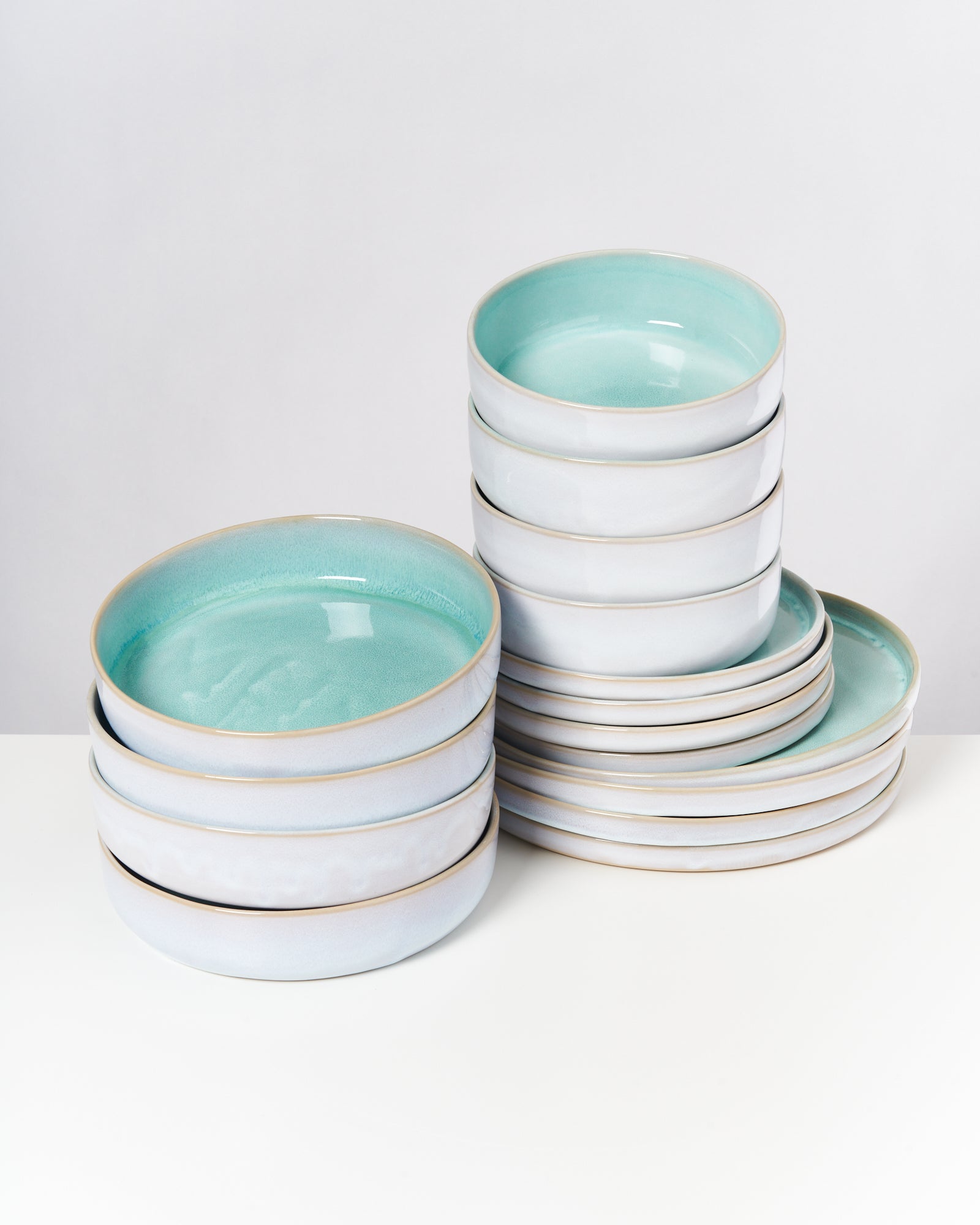 Gestapelte, flache Schalen mit türkisfarbener Innenfläche und weißen Außenseiten auf einem weißen Untergrund.