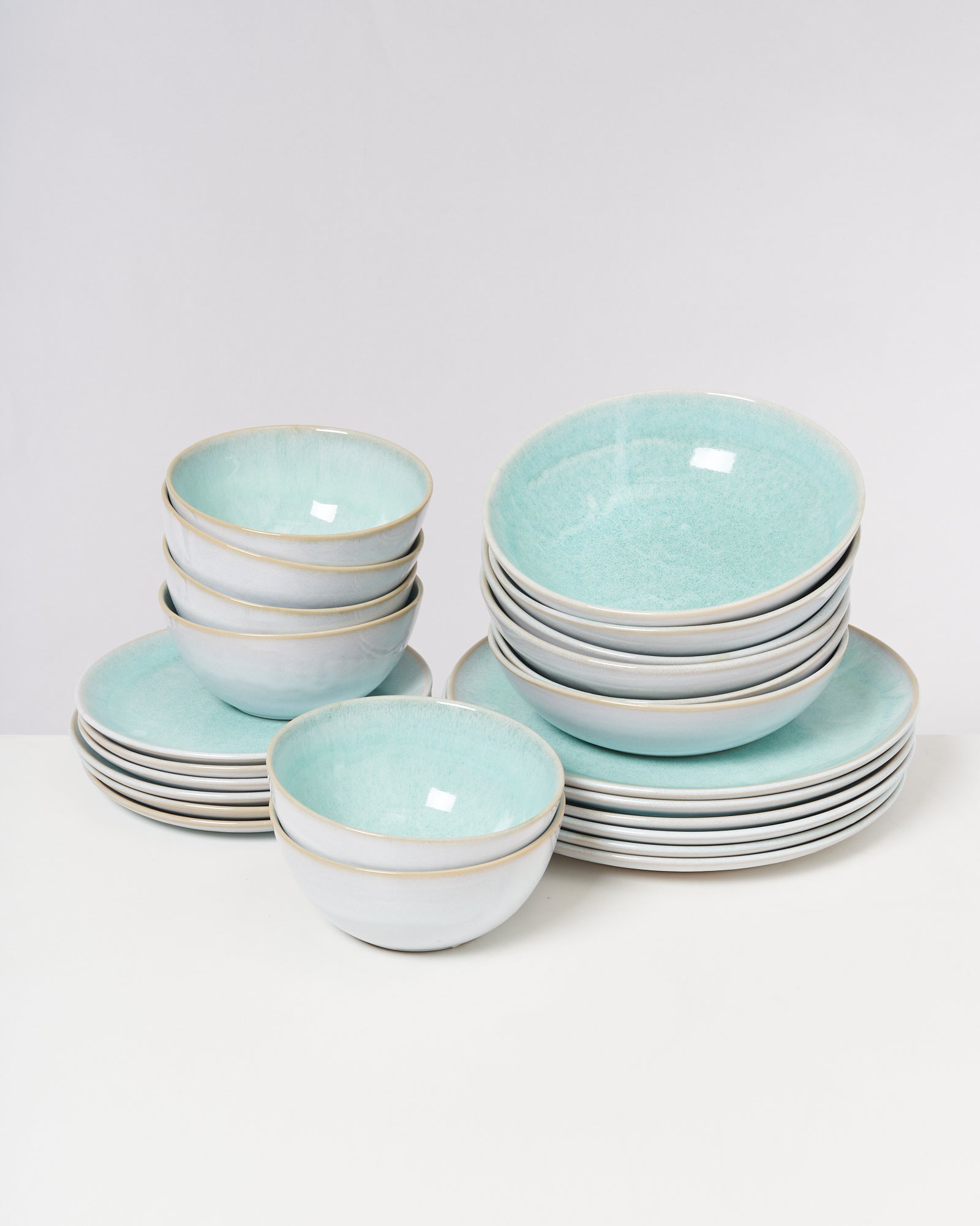 Ein Stapel aus türkisfarbenen Keramikschalen und Tellern auf einer weißen Fläche.