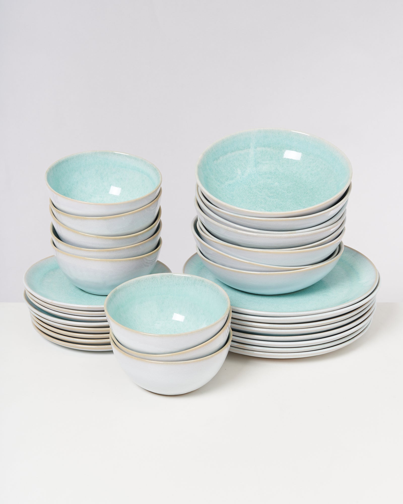Ein Set aus türkisfarbenen und weißen Schüsseln und Tellern ist auf einem weißen Tisch gestapelt.