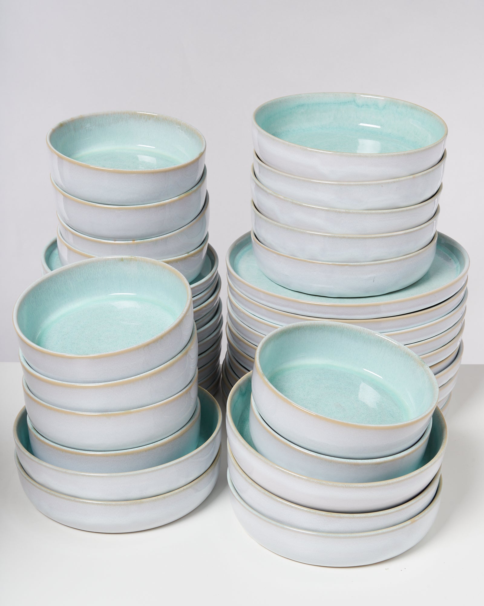 Mehrere gestapelte türkis-weiße Keramikschalen auf einem weißen Untergrund.