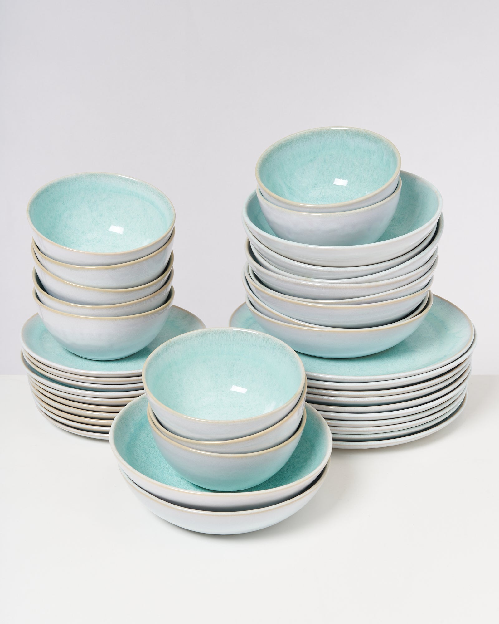 Mehrere Stapel aus türkisfarbenen Schalen und Tellern auf einem weißen Hintergrund.