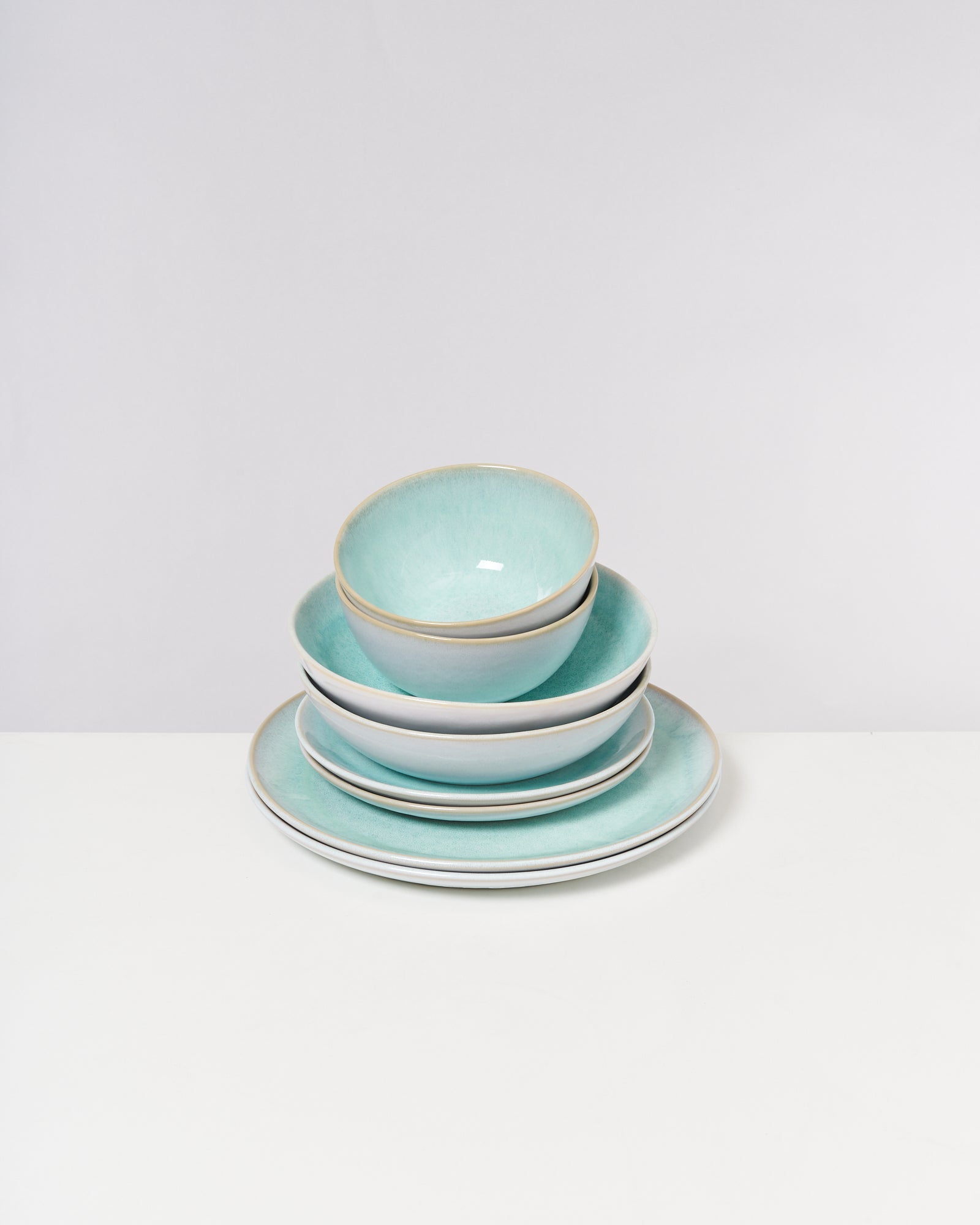 Ein Stapel von drei türkisfarbenen, runden Tellern und zwei Schalen auf einem weißen Hintergrund.