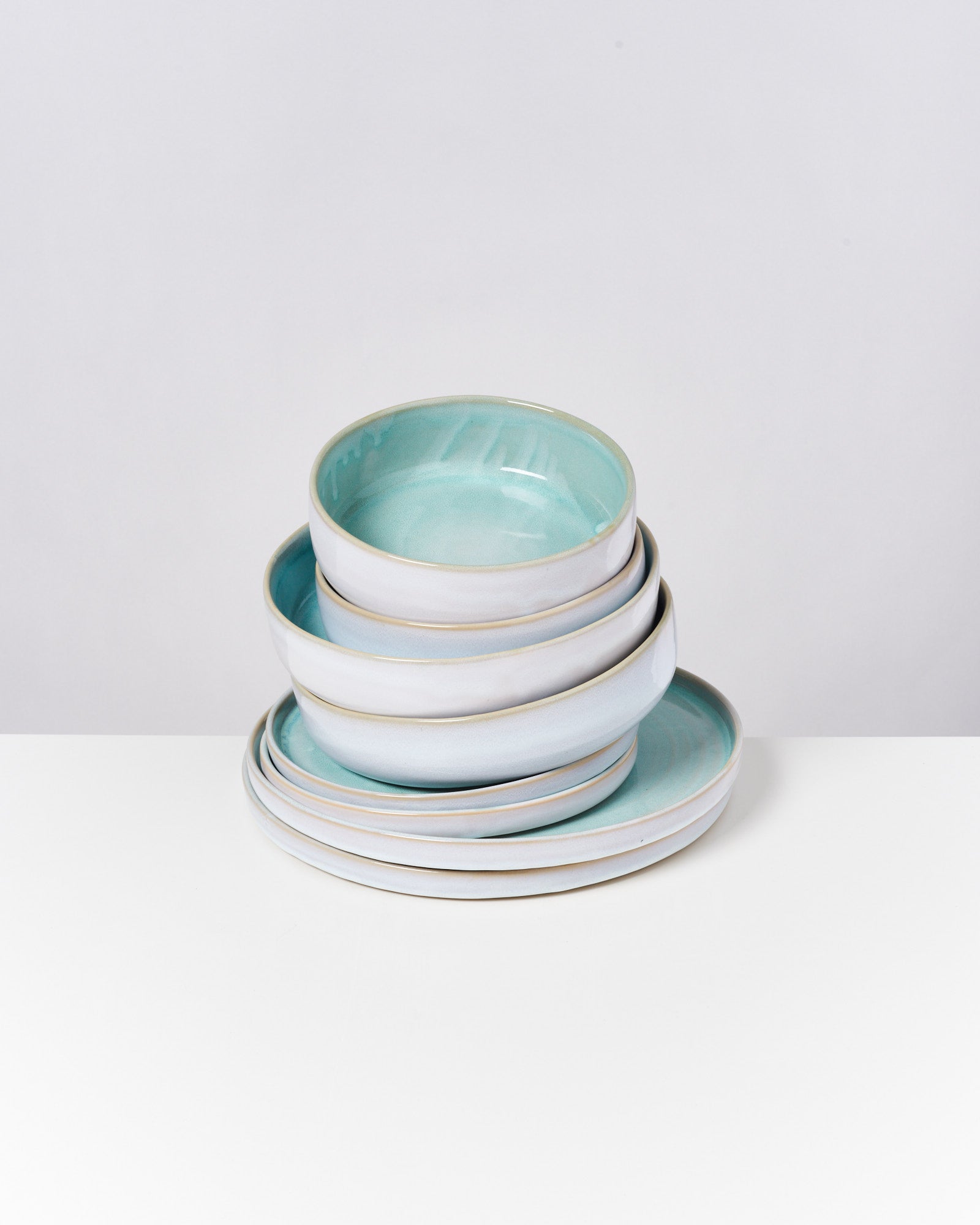Ein Stapel von Keramikschalen und Tellern mit mintgrüner Innenseite auf einem weißen Untergrund.