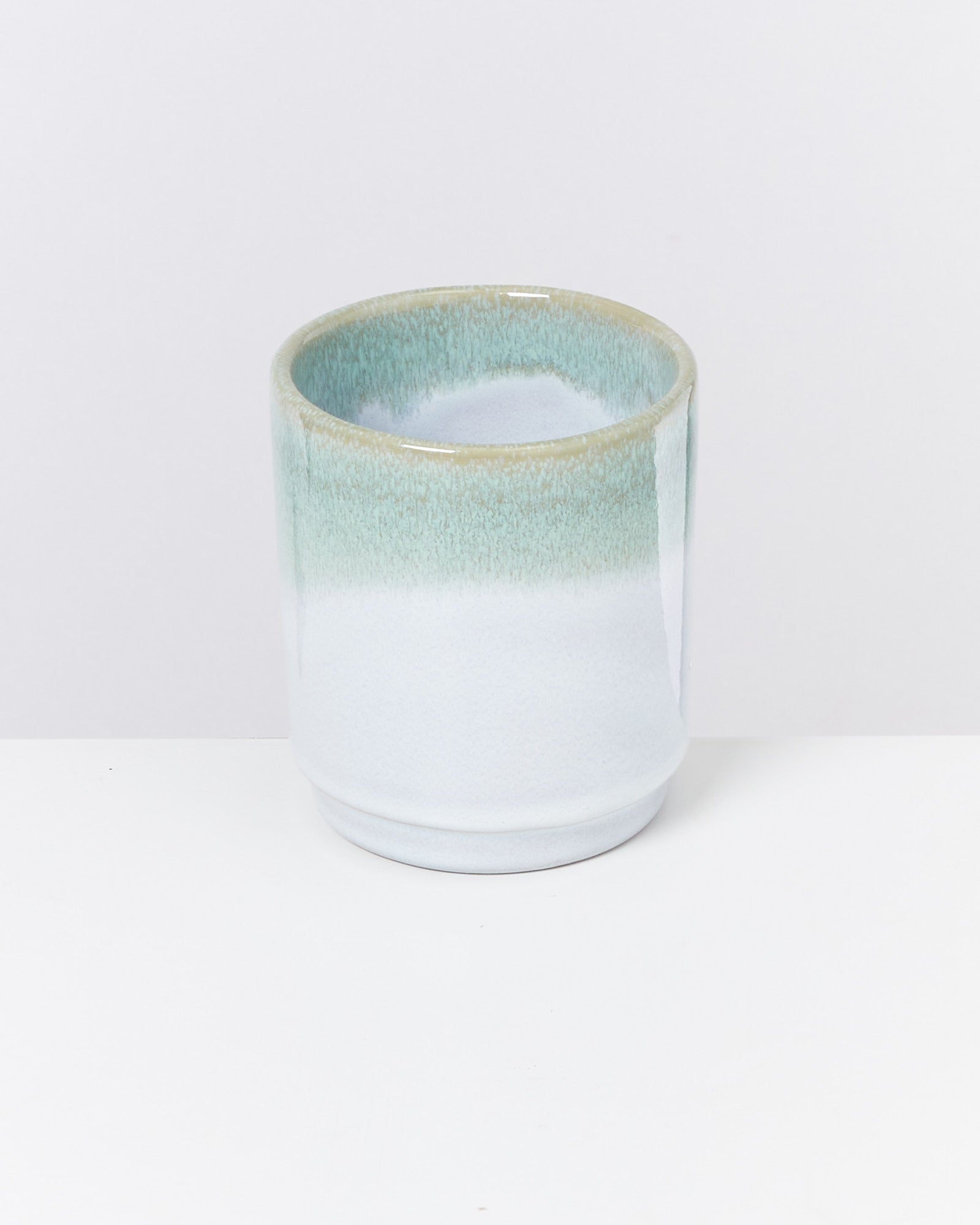 Keramiktasse mit blau-grünem Farbverlauf auf weißem Hintergrund.