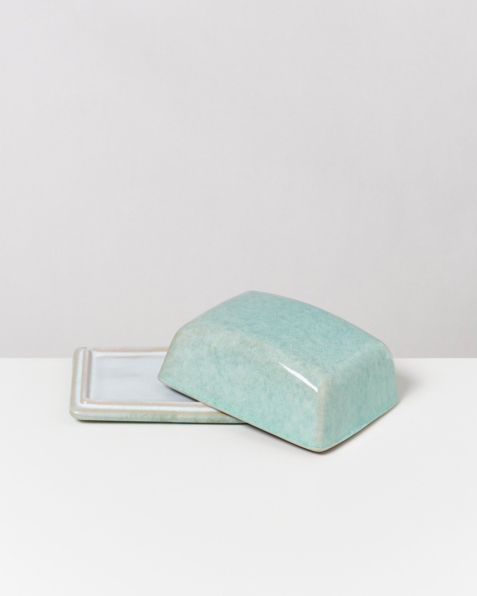 Grüne Keramik-Butterdose auf einem weißen Tisch.