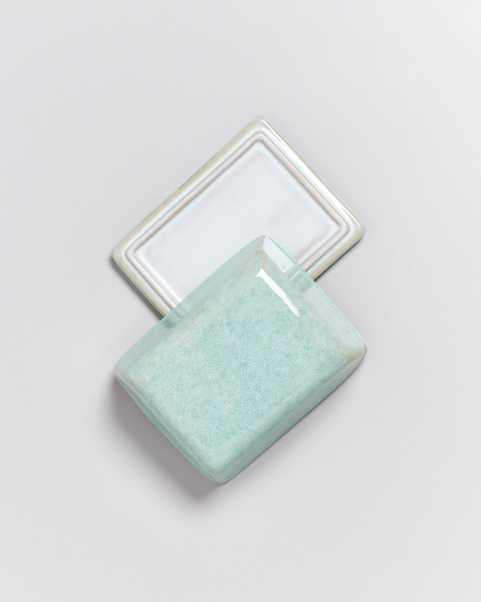 Zwei rechteckige Keramikplatten, eine in hellem Blaugrün und die andere in Weiß, auf einem grauen Hintergrund.