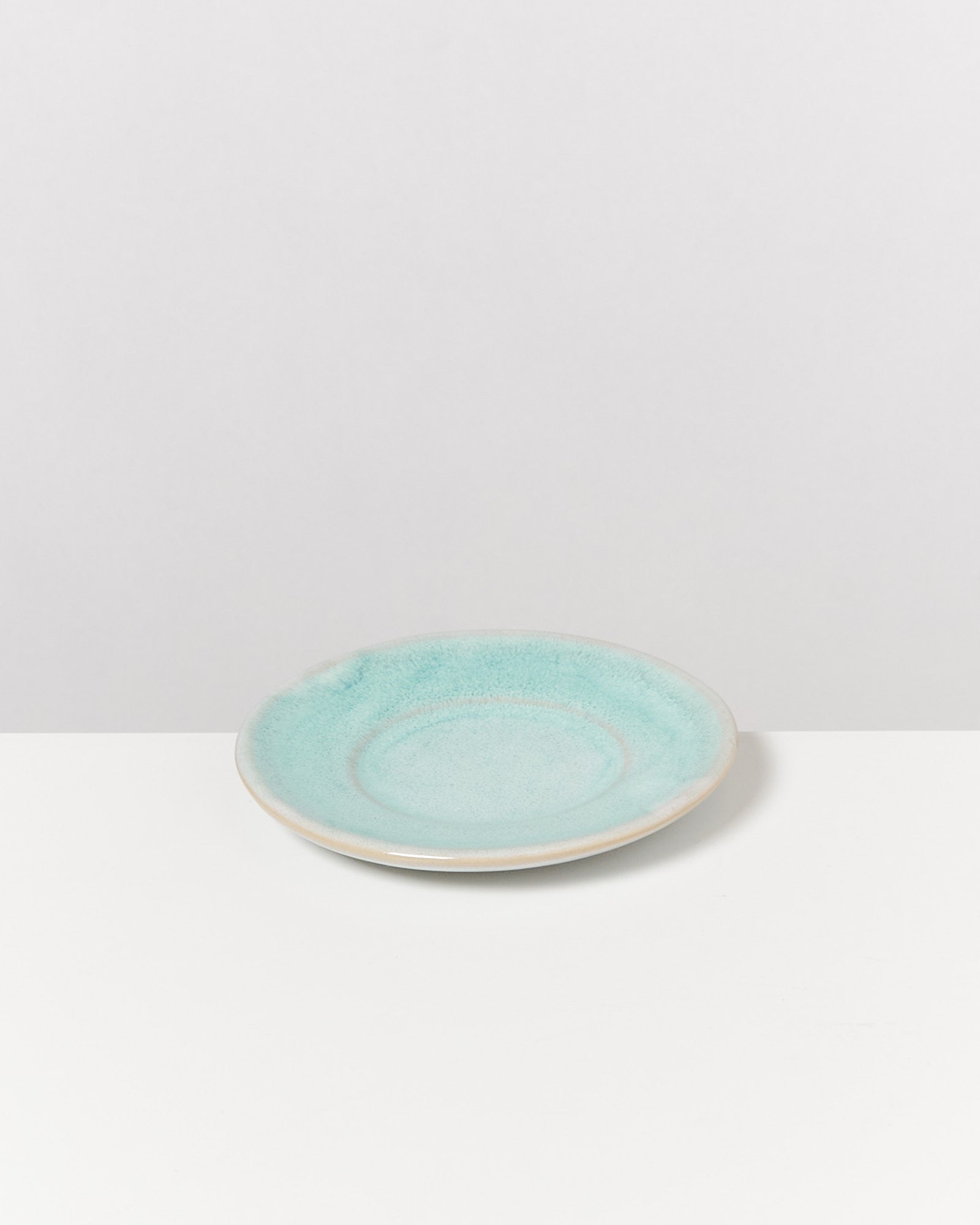 Ein blauer Keramikteller mit hellerem Rand steht auf einem weißen Tisch vor einem grauen Hintergrund.