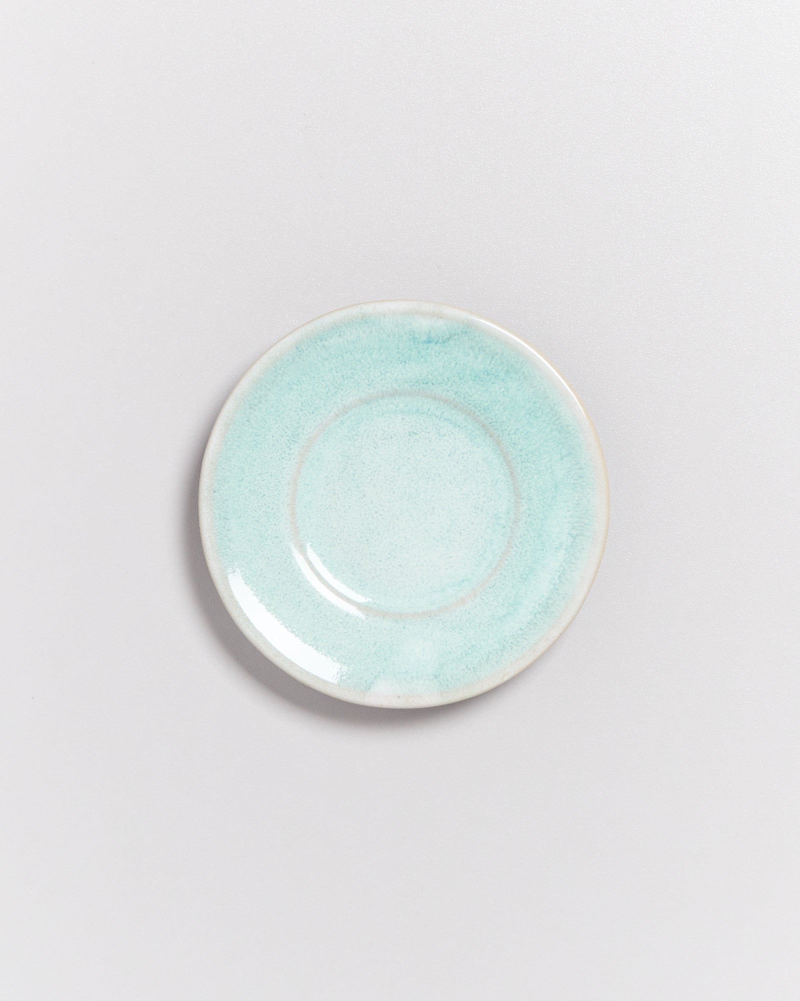 Ein türkisfarbener, runder Teller mit glattem Rand auf einem hellgrauen Hintergrund.