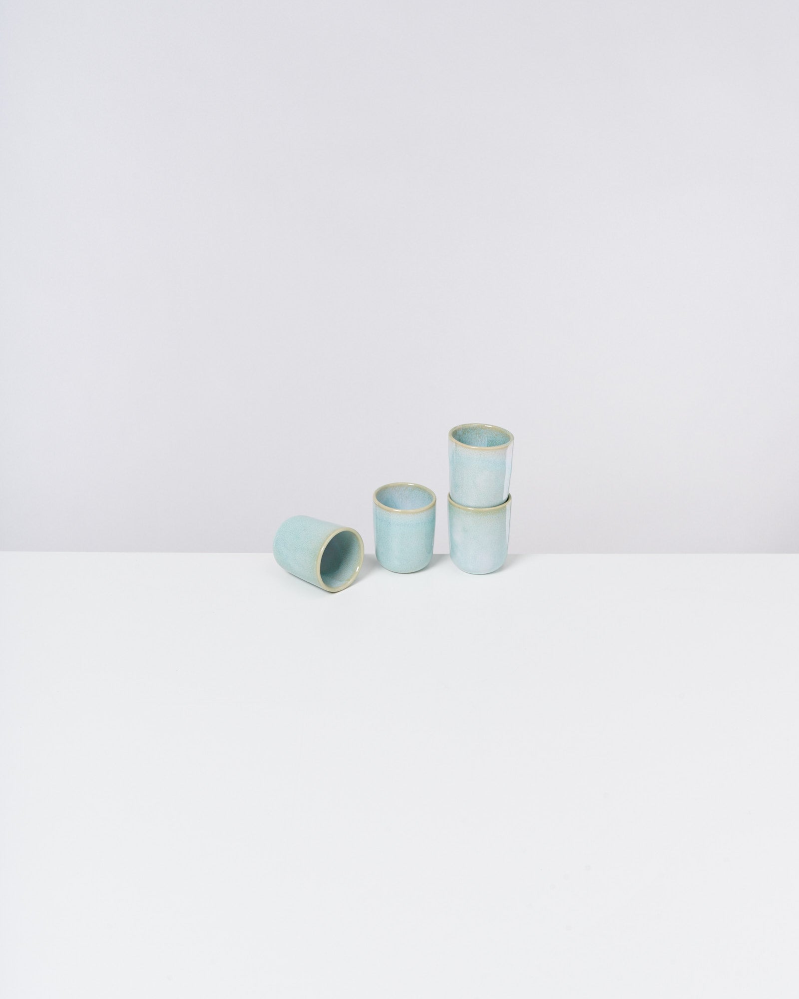 Fünf hellblaue Becher, vier gestapelt und einer daneben liegend, auf weißem Hintergrund.