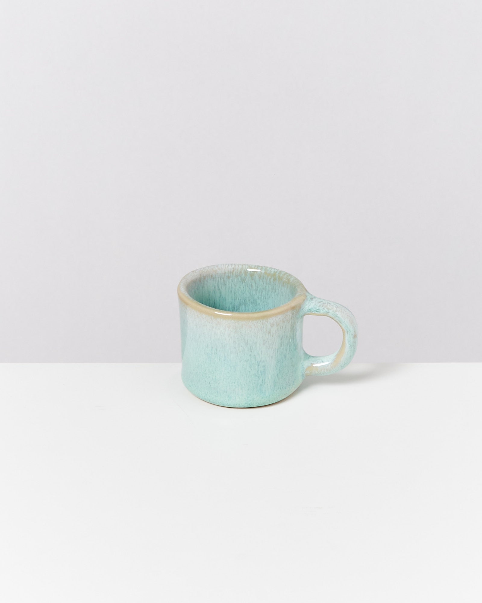 Eine hellblaue Tasse mit Henkel steht auf einem weißen Tisch vor einem grauen Hintergrund.