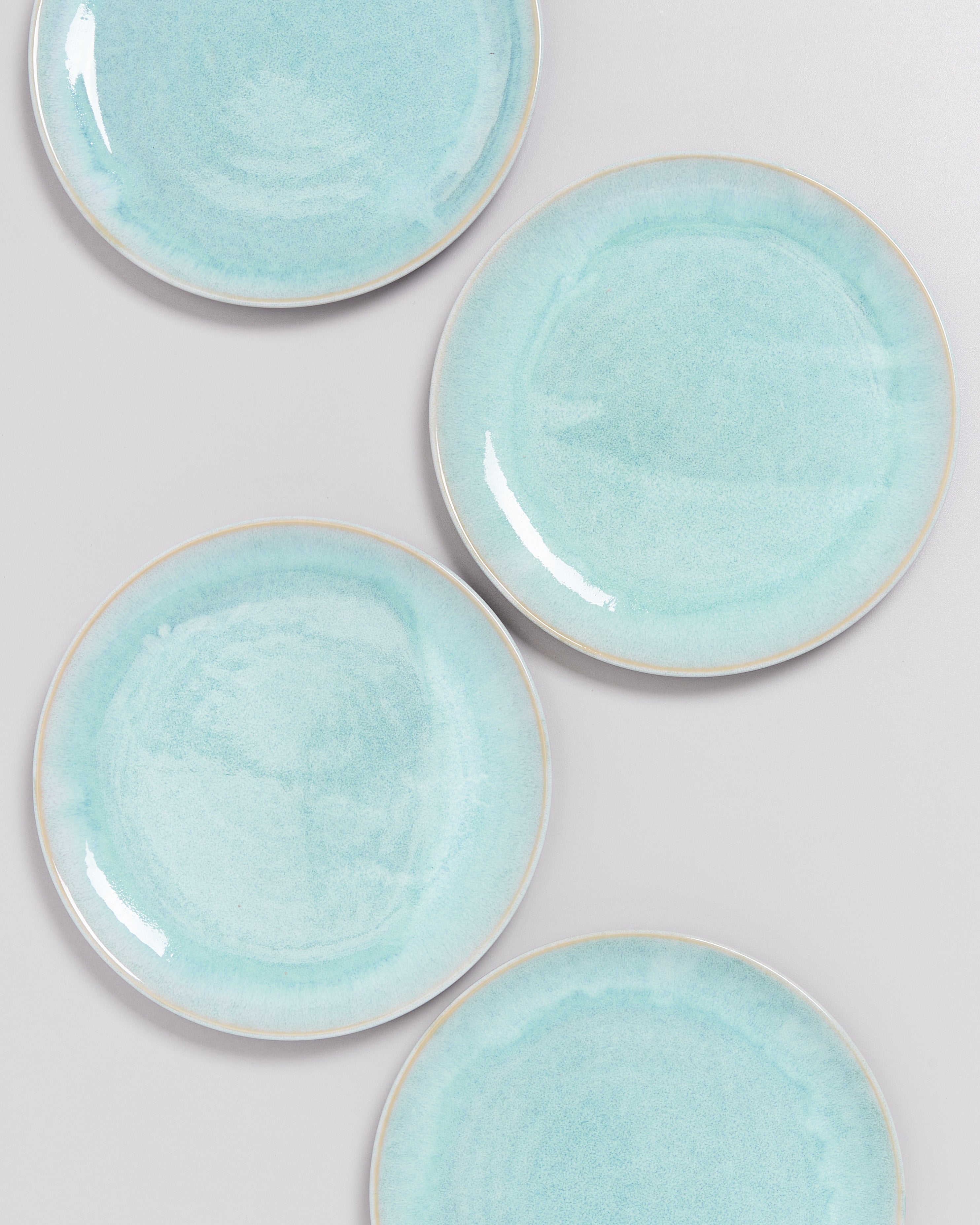 Vier türkisfarbene Teller mit subtilen Mustern liegen auf einem hellen Hintergrund.