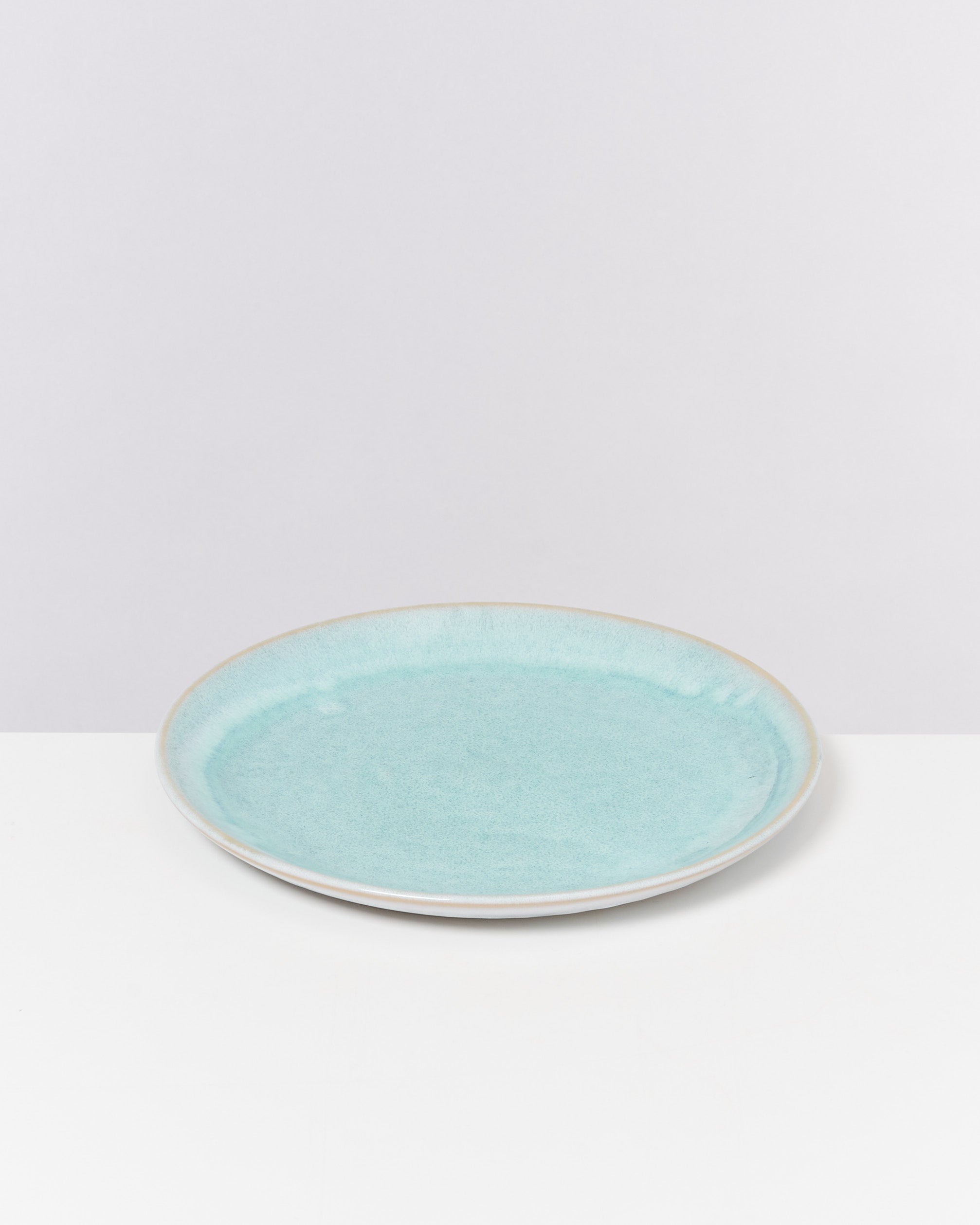 Ein flacher, hellblauer Teller mit glatter Oberfläche auf einem weißen Untergrund.