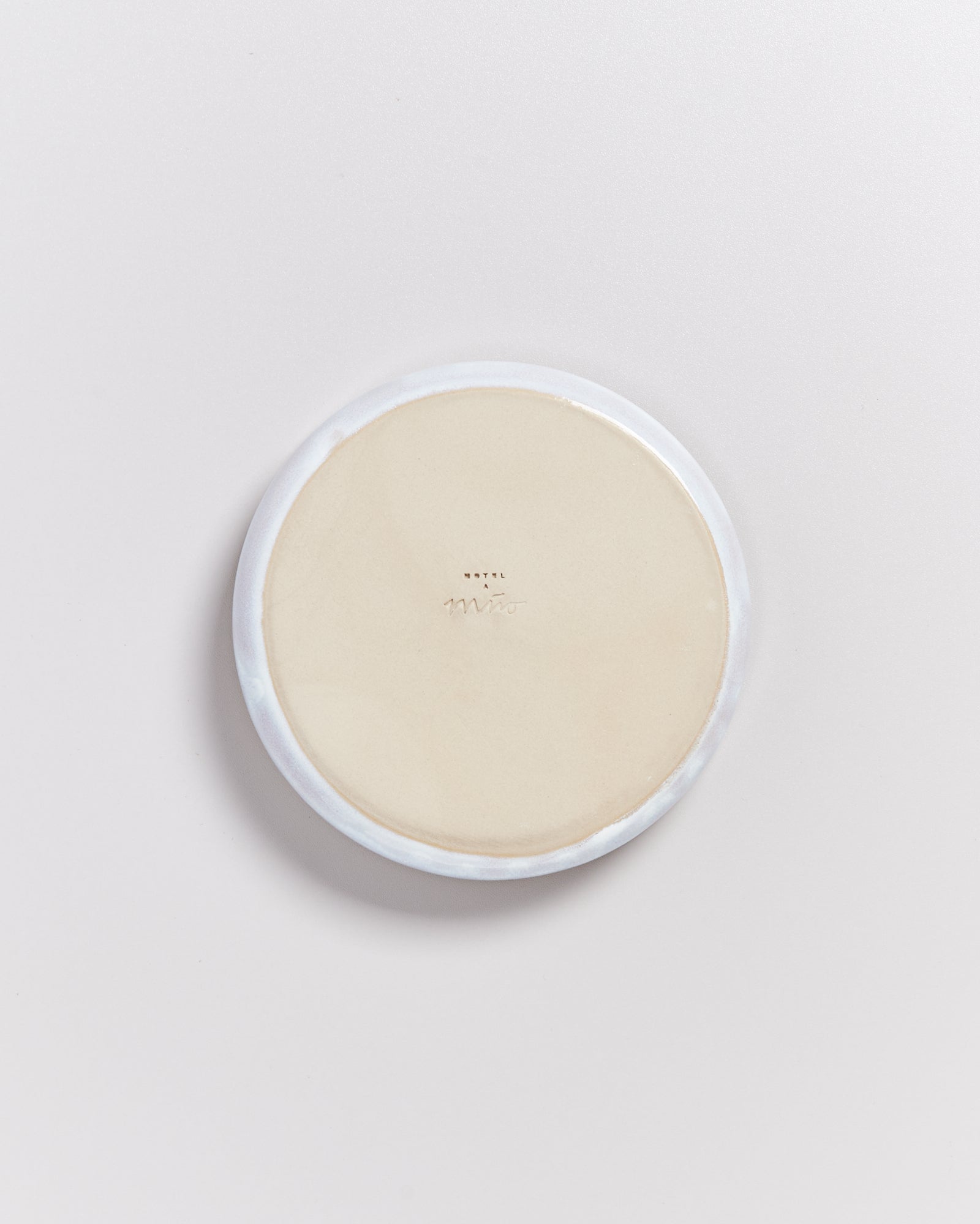 Beiger, runder Gegenstand mit hellerem Rand auf einer weißen Fläche.