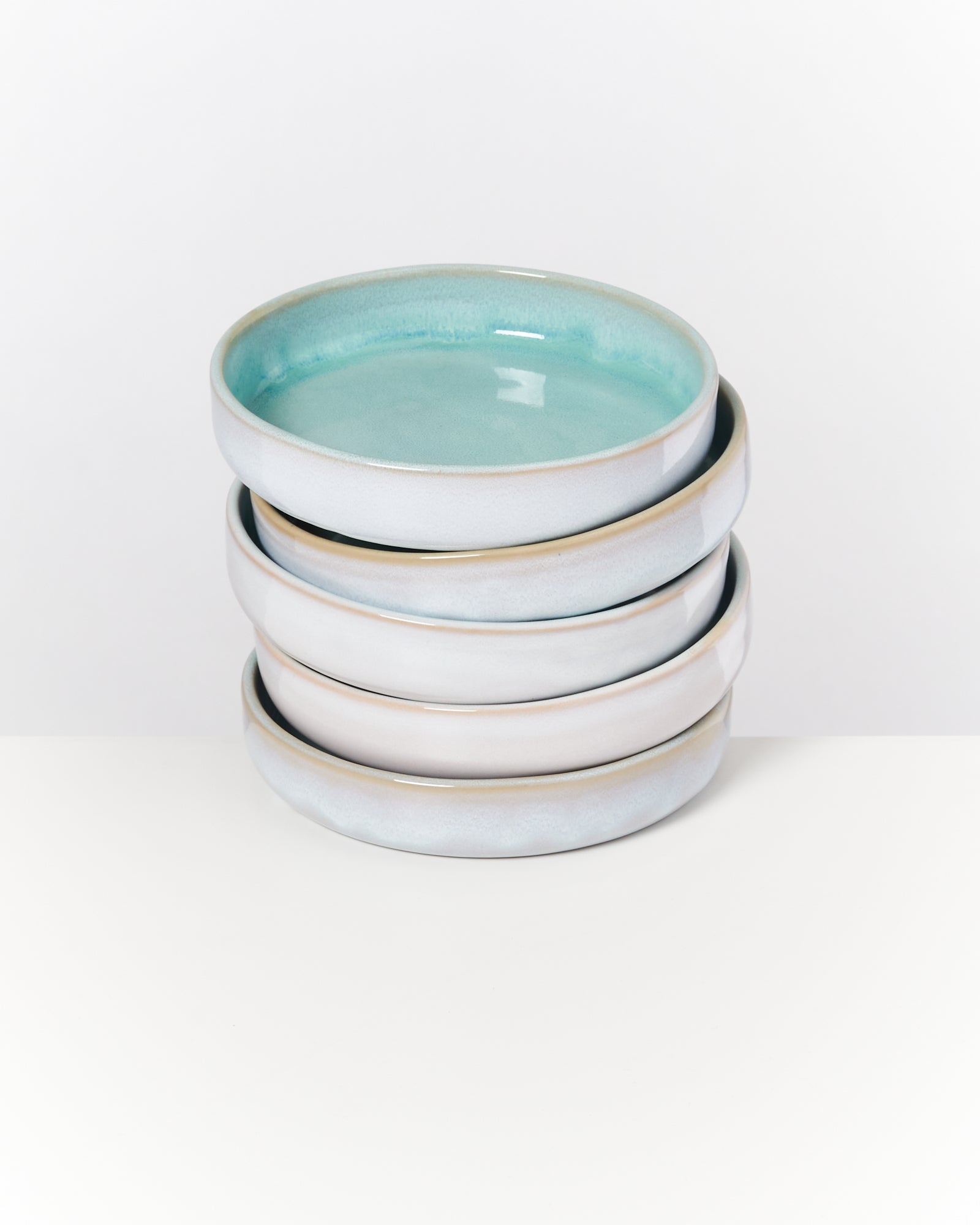 Ein Stapel von vier runden Keramikschalen mit blau-grüner Glasur auf einem weißen Untergrund.