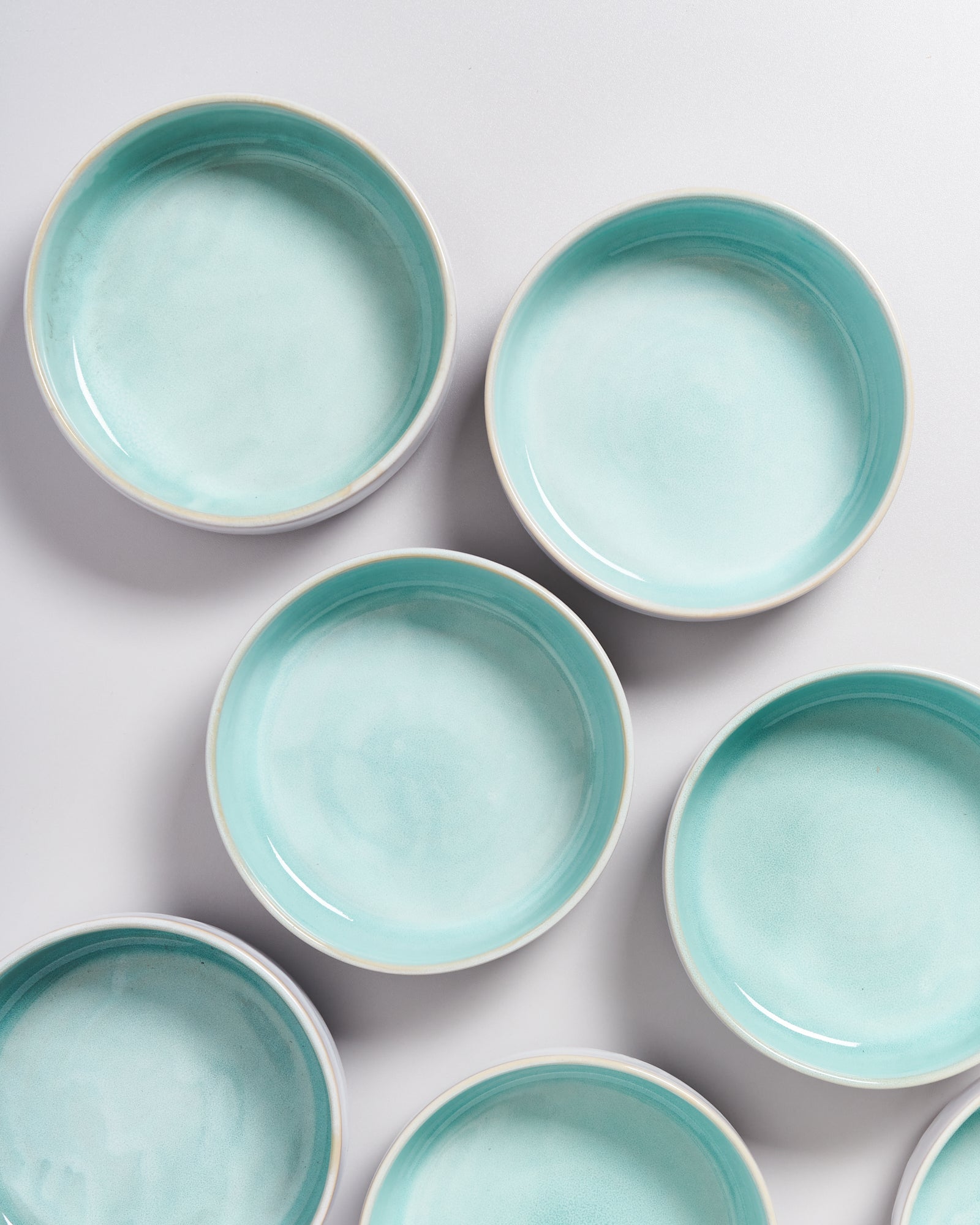 Acht türkisfarbene Keramikschalen auf einer weißen Oberfläche.
