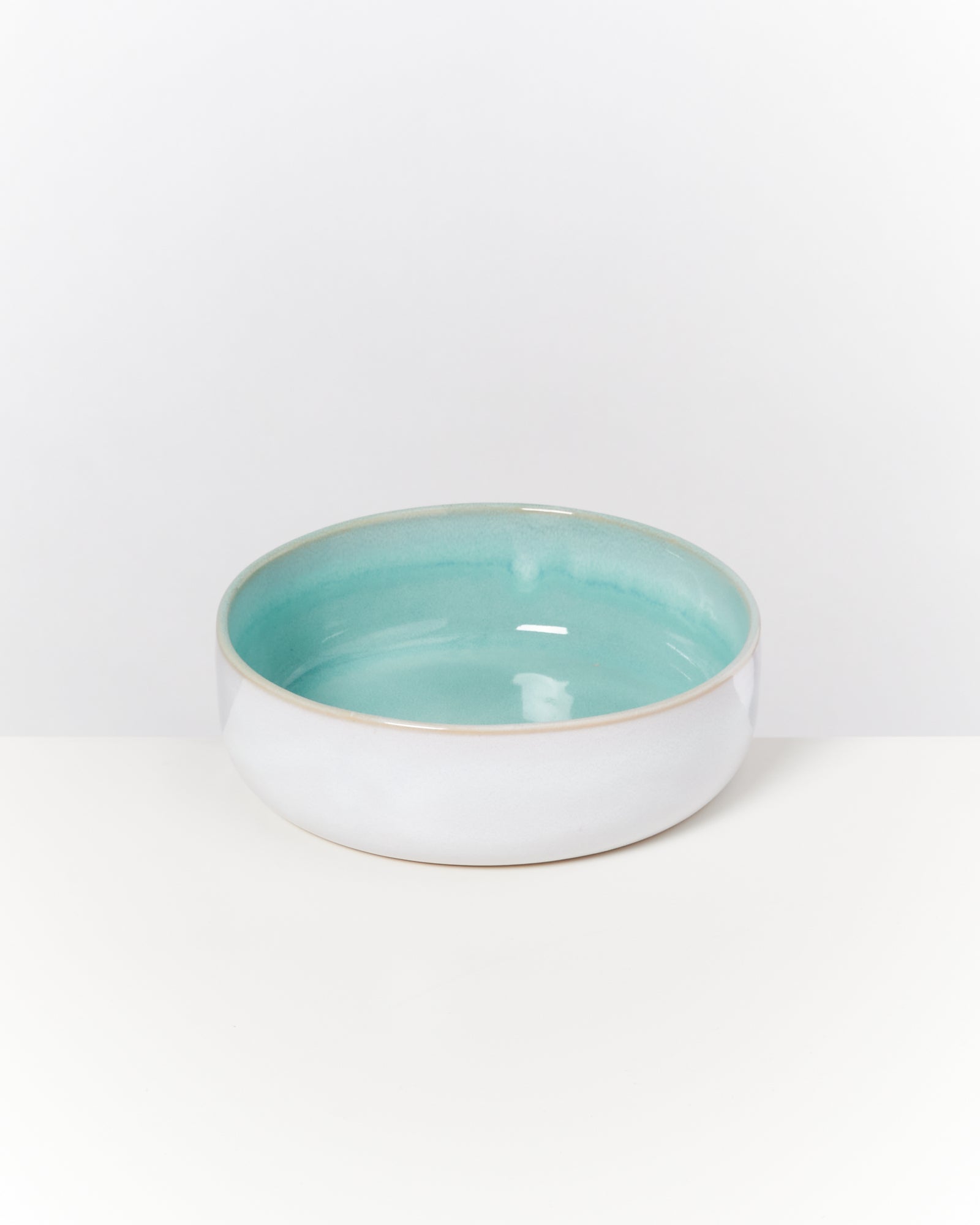Weiße Keramikschüssel mit türkisfarbenem Inneren auf weißem Hintergrund.