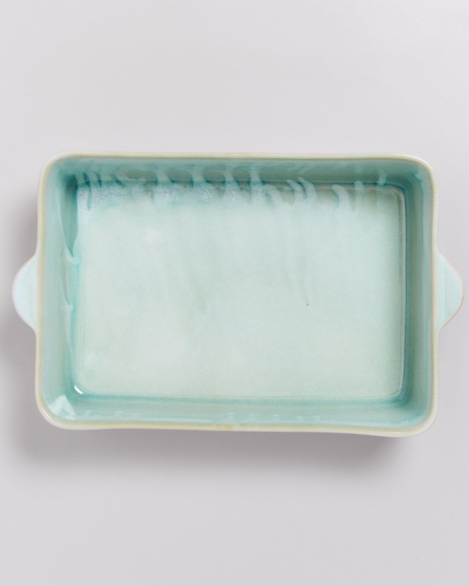 Rechteckige, helltürkis glasierte Keramikschale mit zwei seitlichen Griffen auf einer weißen Oberfläche.