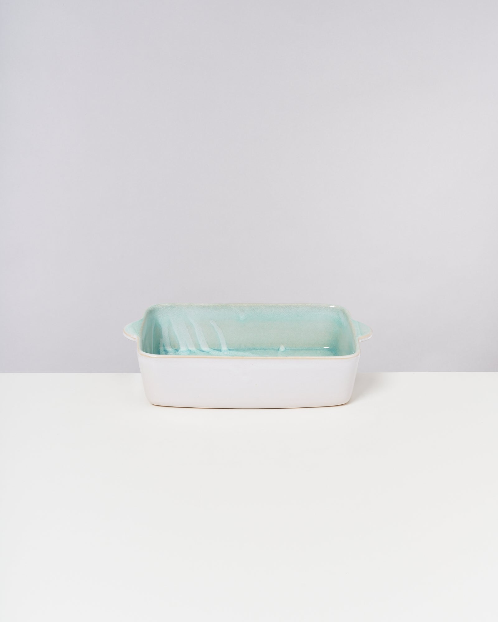 Weiße rechteckige Auflaufform mit helltürkiser Innenseite auf weißem Tisch vor grauem Hintergrund.