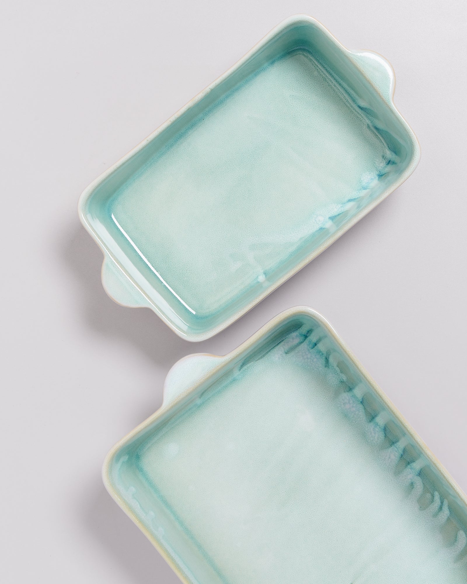 Zwei rechteckige, türkisfarbene Keramik-Auflaufformen auf einem hellen Hintergrund.