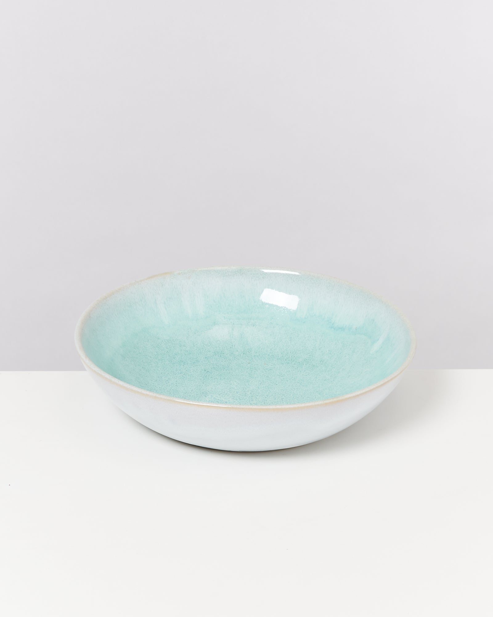 Eine flache Schüssel mit hellblauer Glasur steht auf einem weißen Hintergrund.