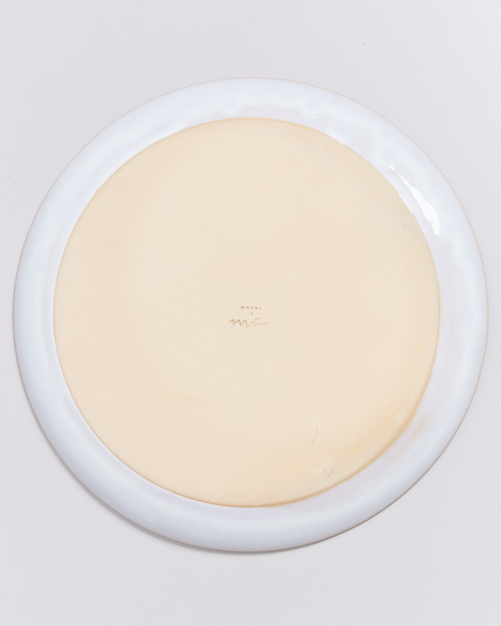 Rückseite eines weißen Tellers mit einem beigen Rand, auf hellem Hintergrund.