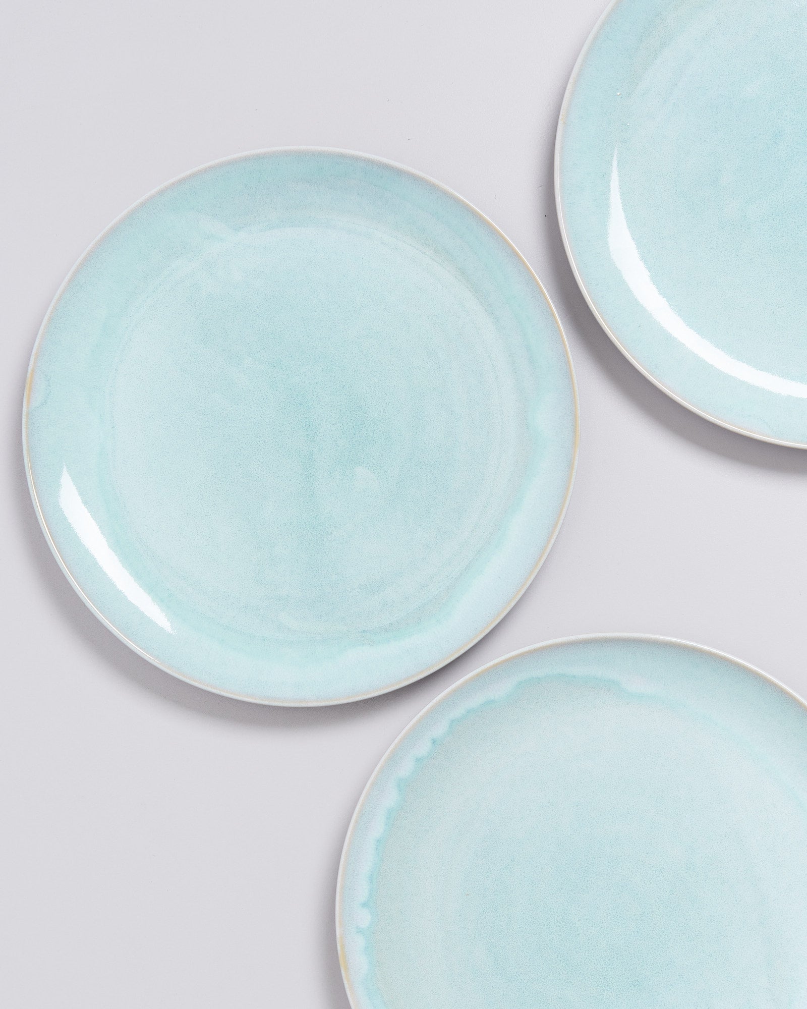 Drei runde, pastellblaue Teller auf einem hellgrauen Hintergrund.