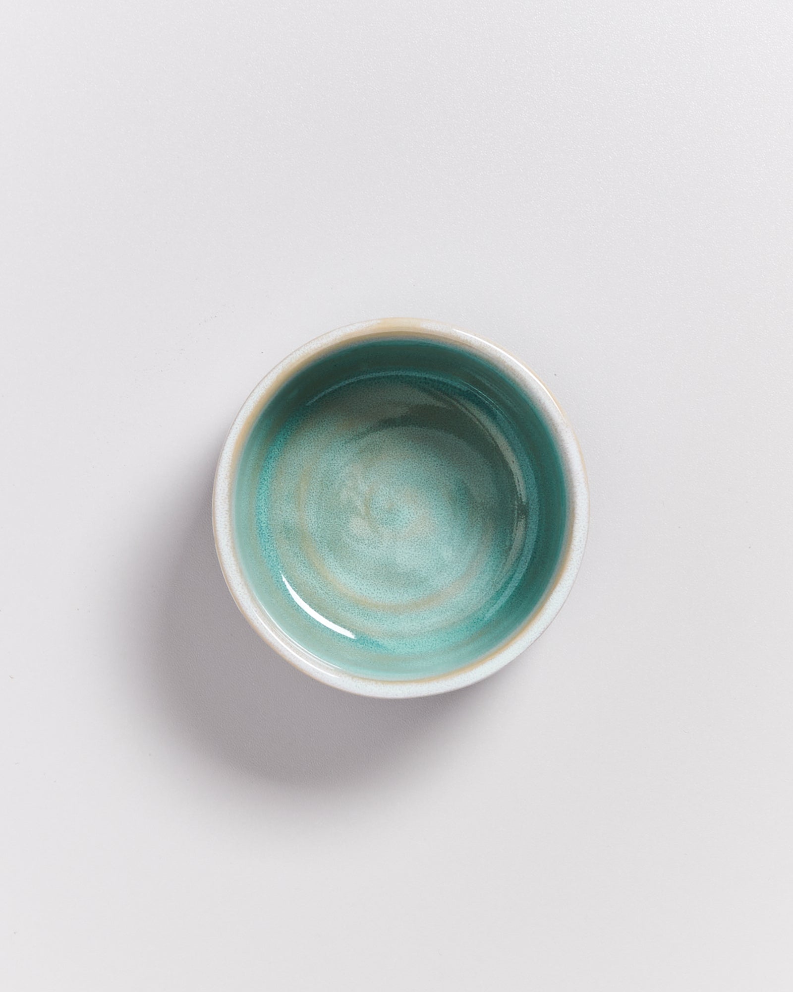 Ein kleiner, runder, türkisfarbener Keramikschüssel auf weißem Hintergrund.