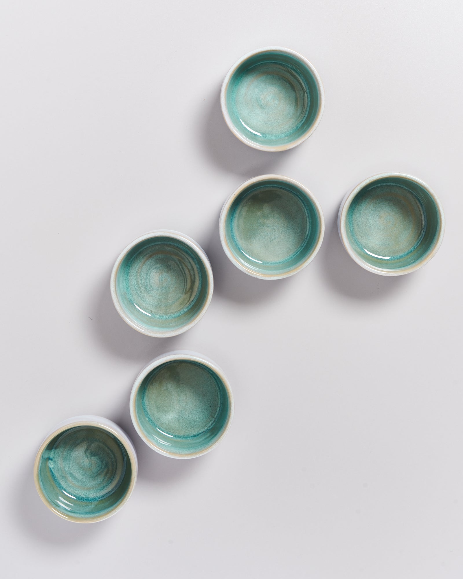 Sechs türkisfarbene Schalen sind diagonal auf einem weißen Hintergrund angeordnet.