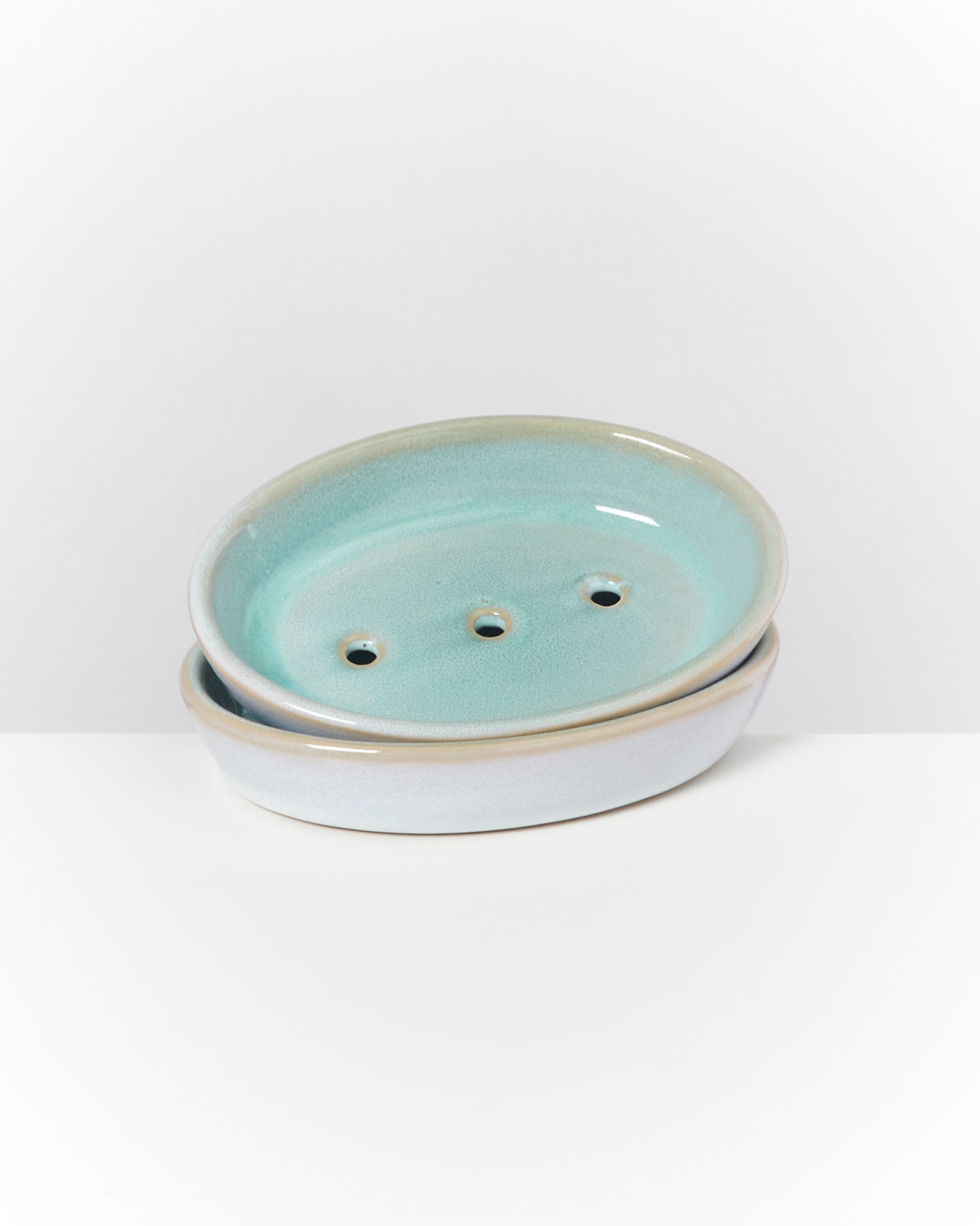 Zwei übereinander gestapelte ovale Seifenschalen aus Keramik mit blauer Glasur und drei kleinen Löchern.