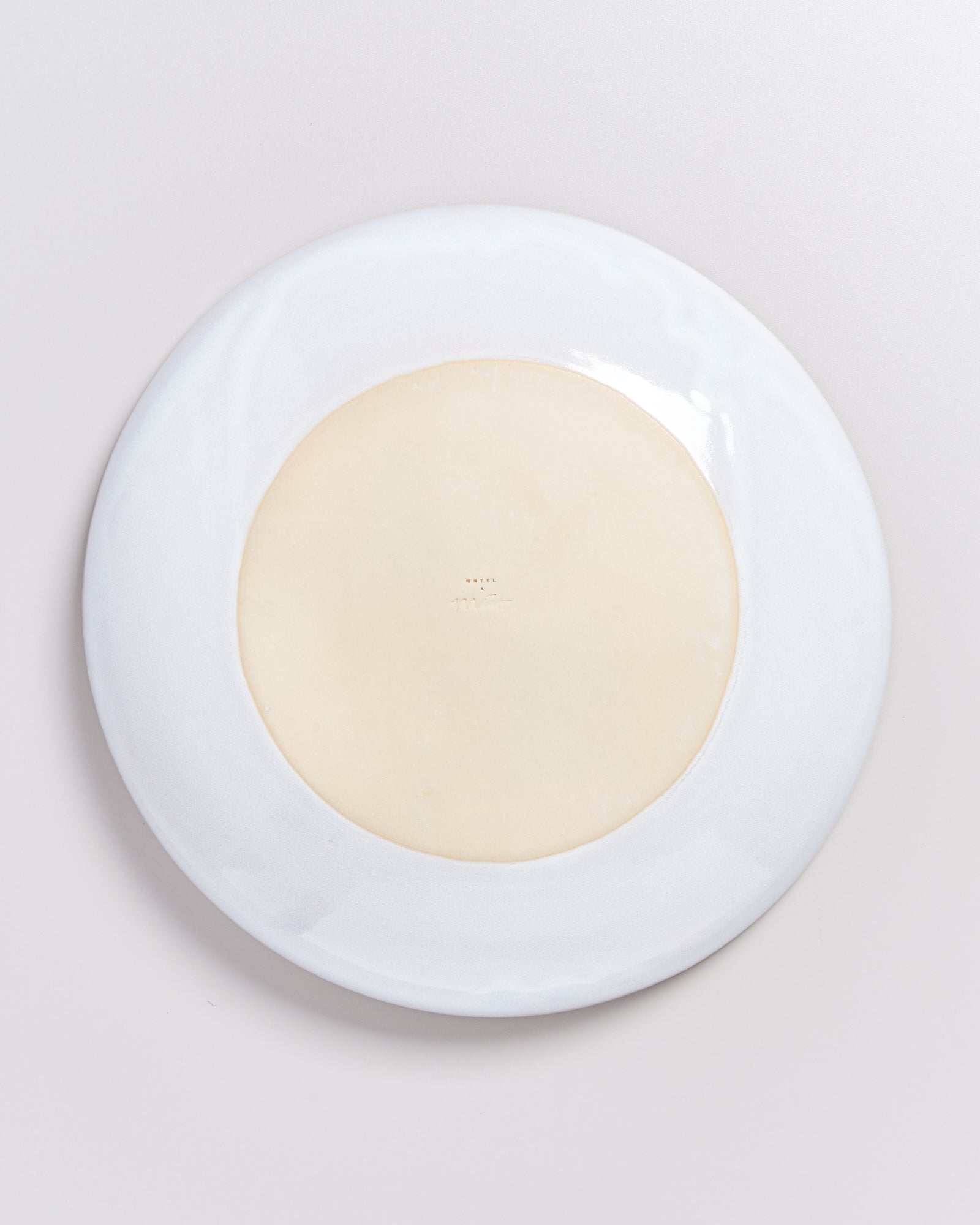 Rückseite eines weißen Tellers auf einer hellen Oberfläche fotografiert.