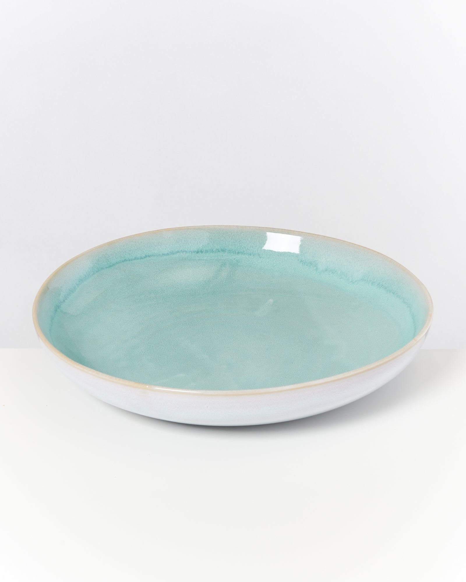 Eine runde, flache Schale mit türkisfarbener Glasur auf weißem Hintergrund.