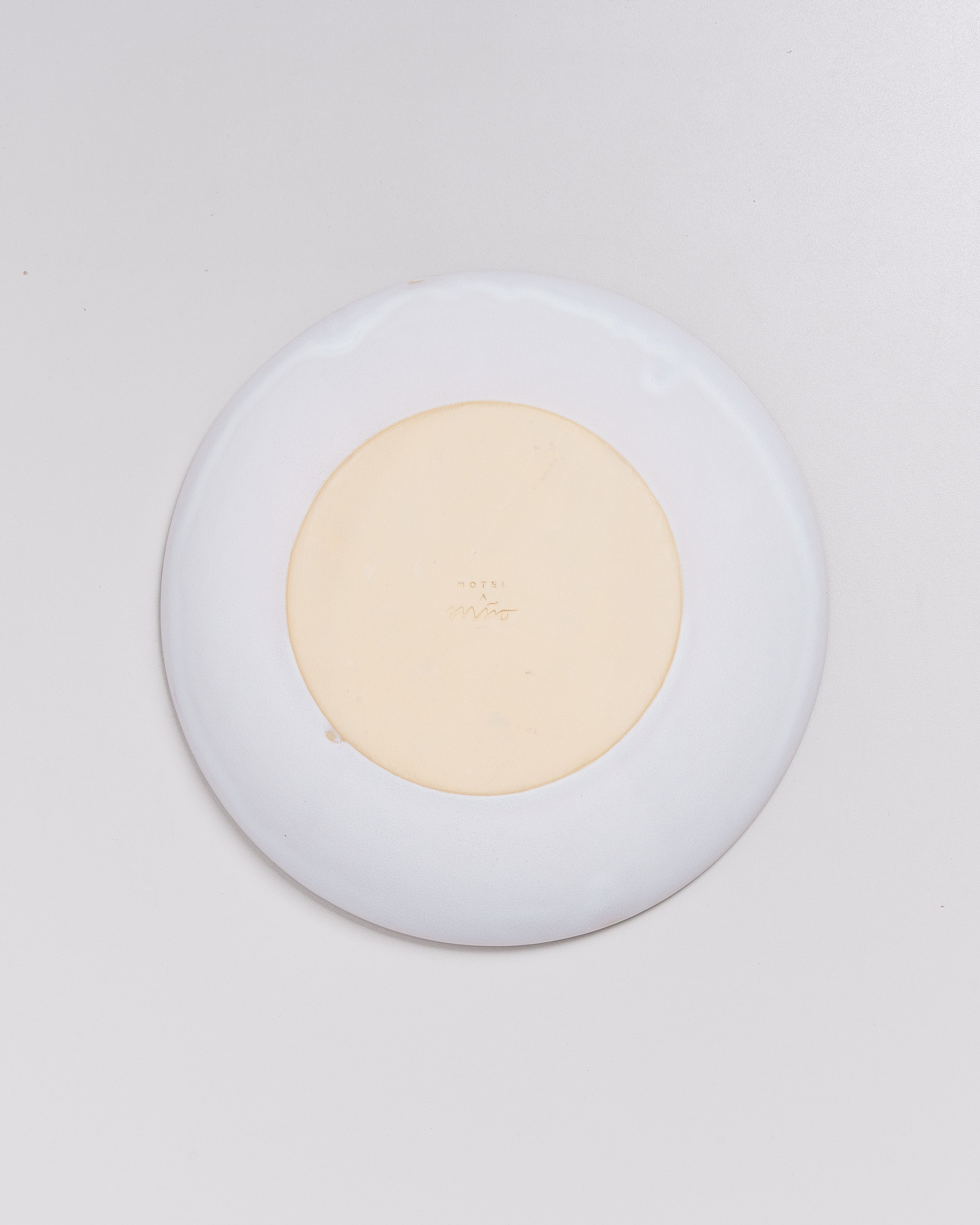 Die Rückseite eines runden weißen und beigefarbenen Tellers mit einer kaum lesbaren Aufschrift in der Mitte.