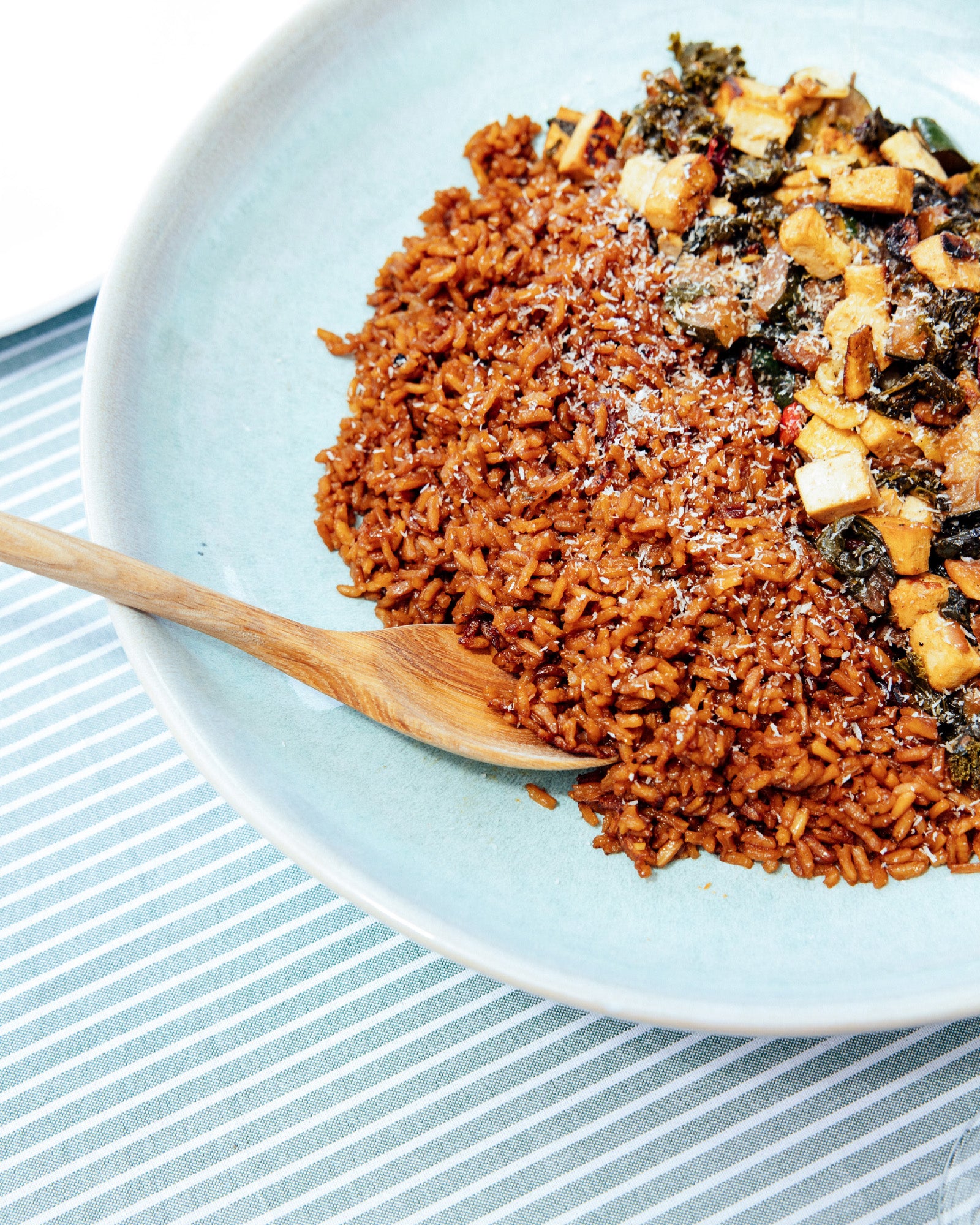 Ein Teller mit würzigem Reis und gebratenem Gemüse auf einem gestreiften Tischtuch.