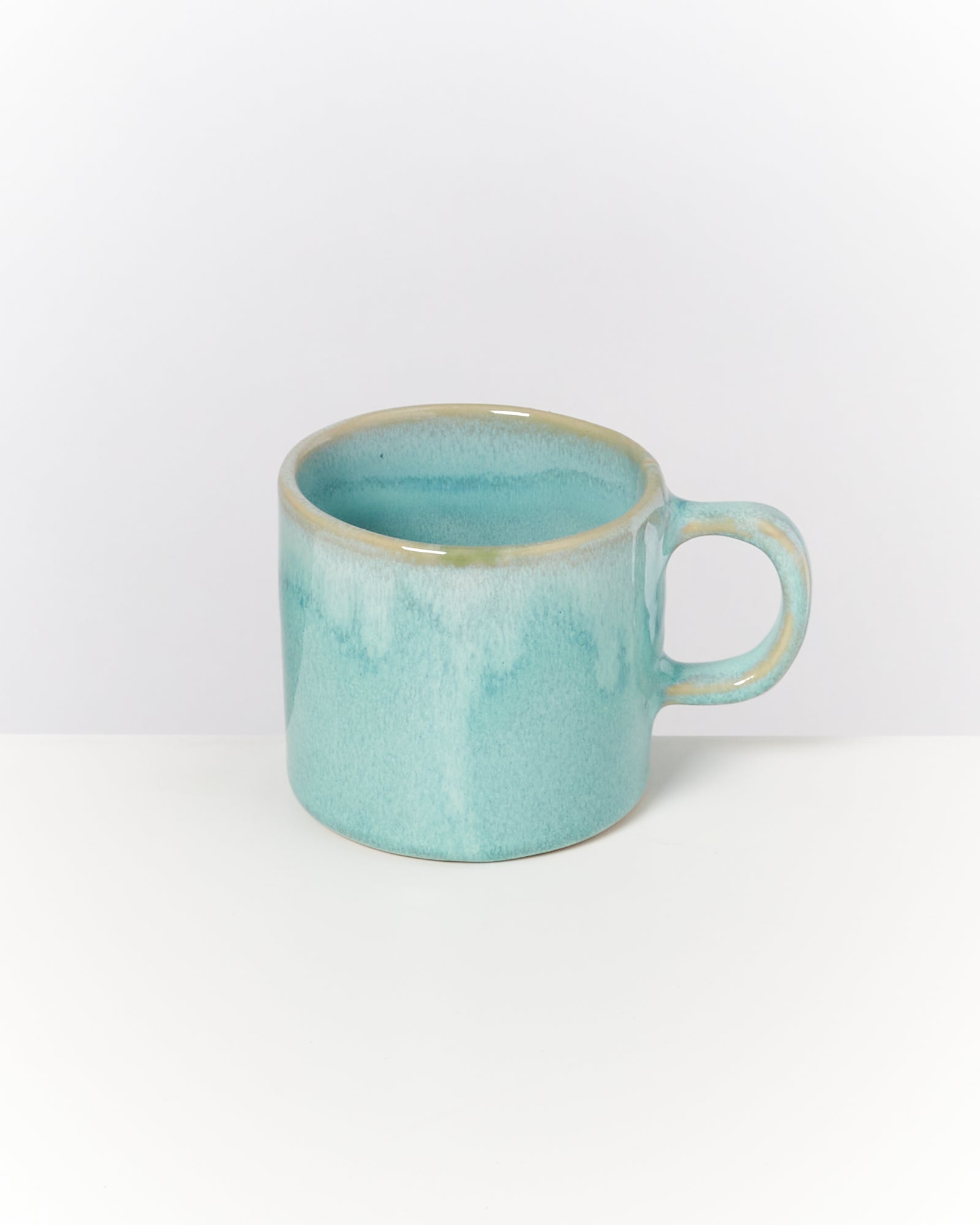 Türkisfarbene Keramiktasse mit Henkel auf weißem Hintergrund.