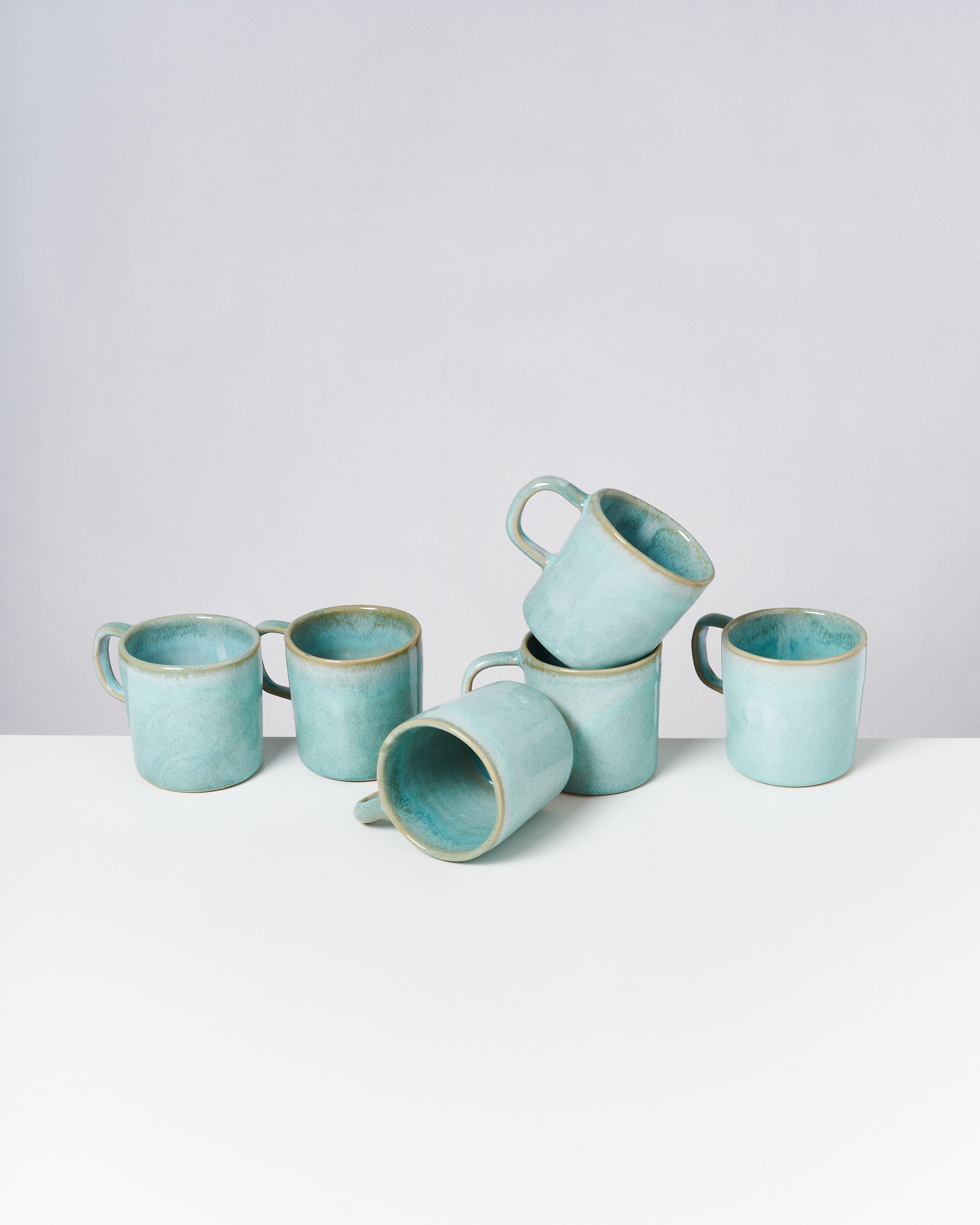 Sechs türkisfarbene Keramiktassen auf weißem Hintergrund, teils gestapelt.