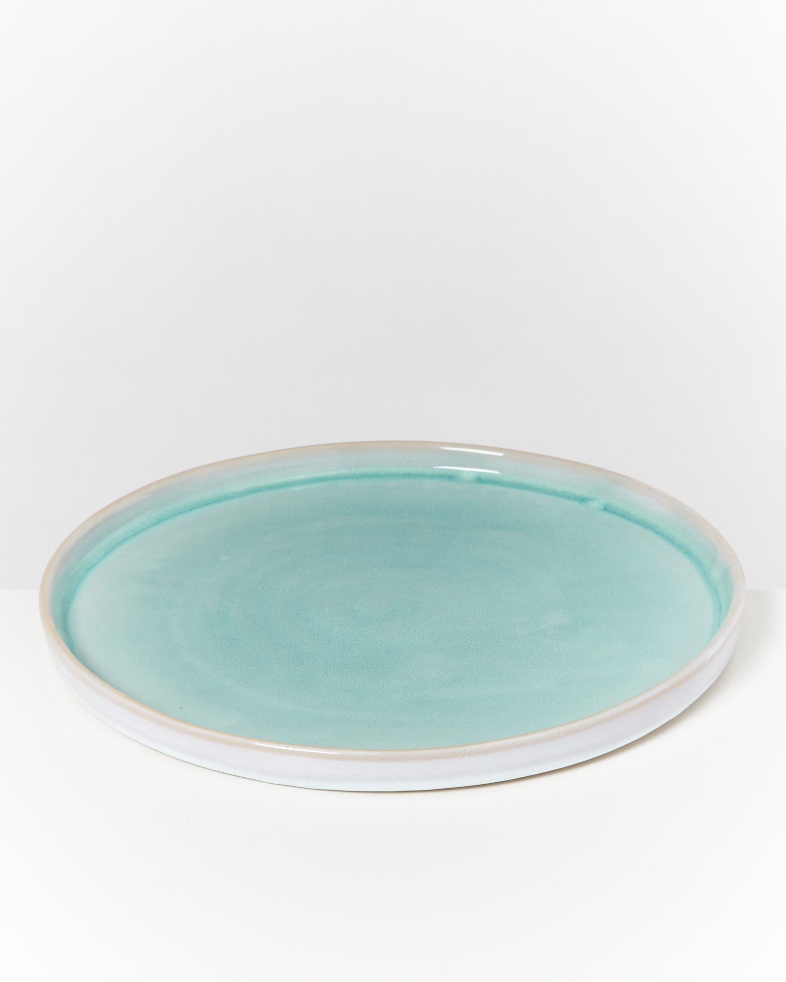 Runder, flacher Teller in türkis mit hellem Rand auf weißem Hintergrund.
